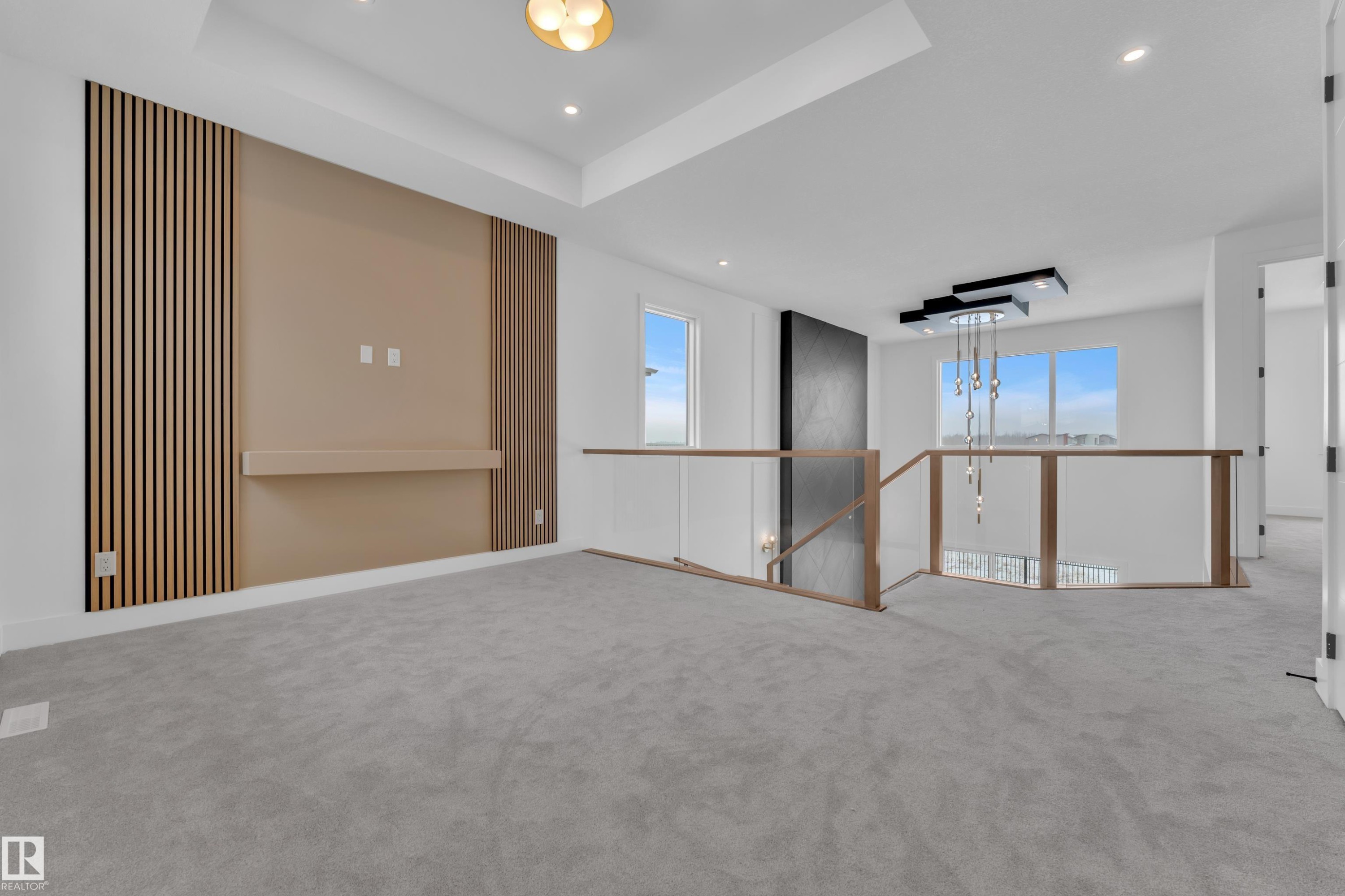 This spacious interior area features light gray carpeting, a decorative wall panel with a built-in shelf, and a contemporary light fixture - 503 Creekside Bay, Leduc, AB - Indoor Photo Showing Other Room