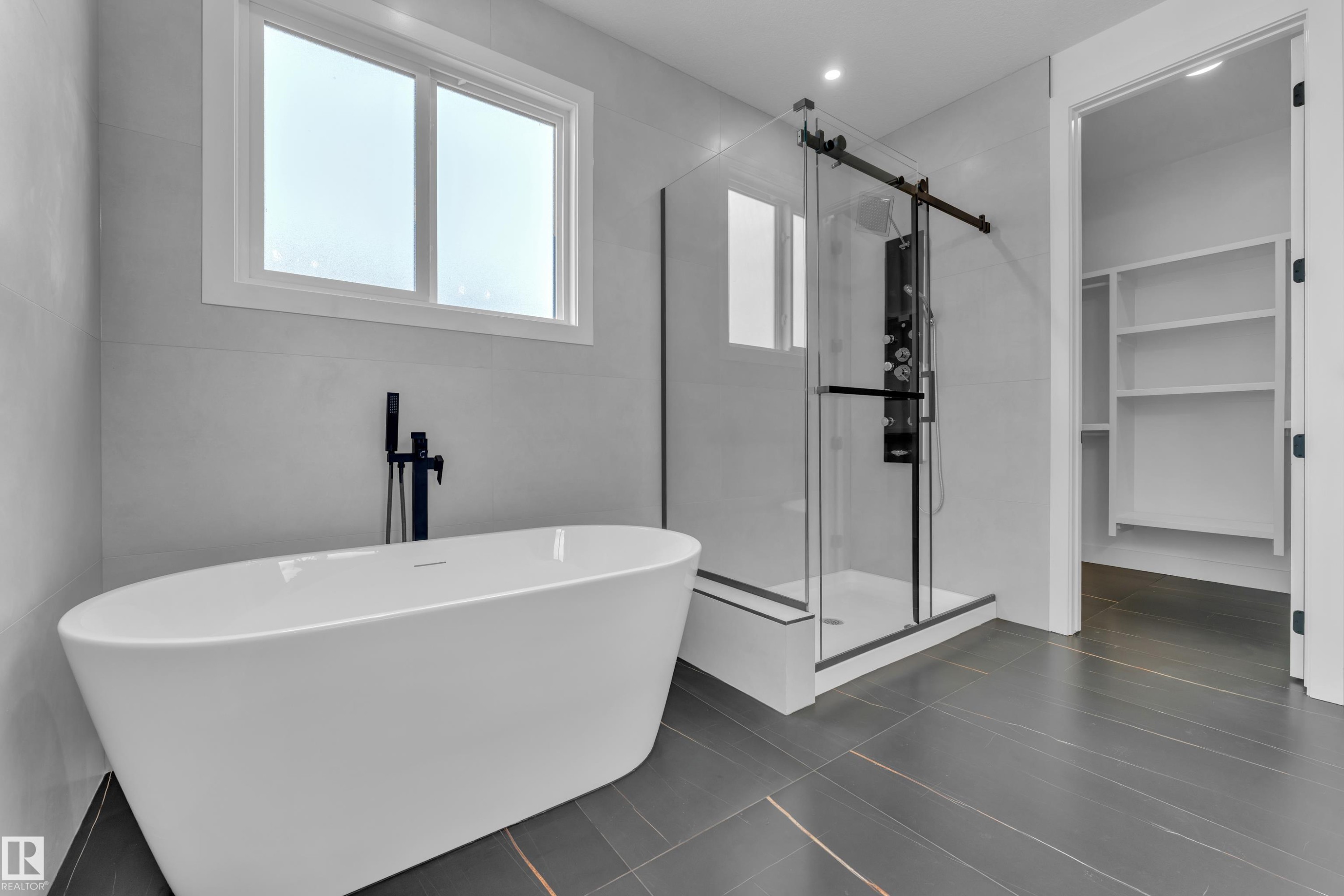 Contemporary bathroom featuring a freestanding soaking tub with a matte black floor-mounted faucet, a walk-in shower with a glass enclosure and matte black fixtures, and dark-toned floor tiles - 503 Creekside Bay, Leduc, AB - Indoor Photo Showing Bathroom