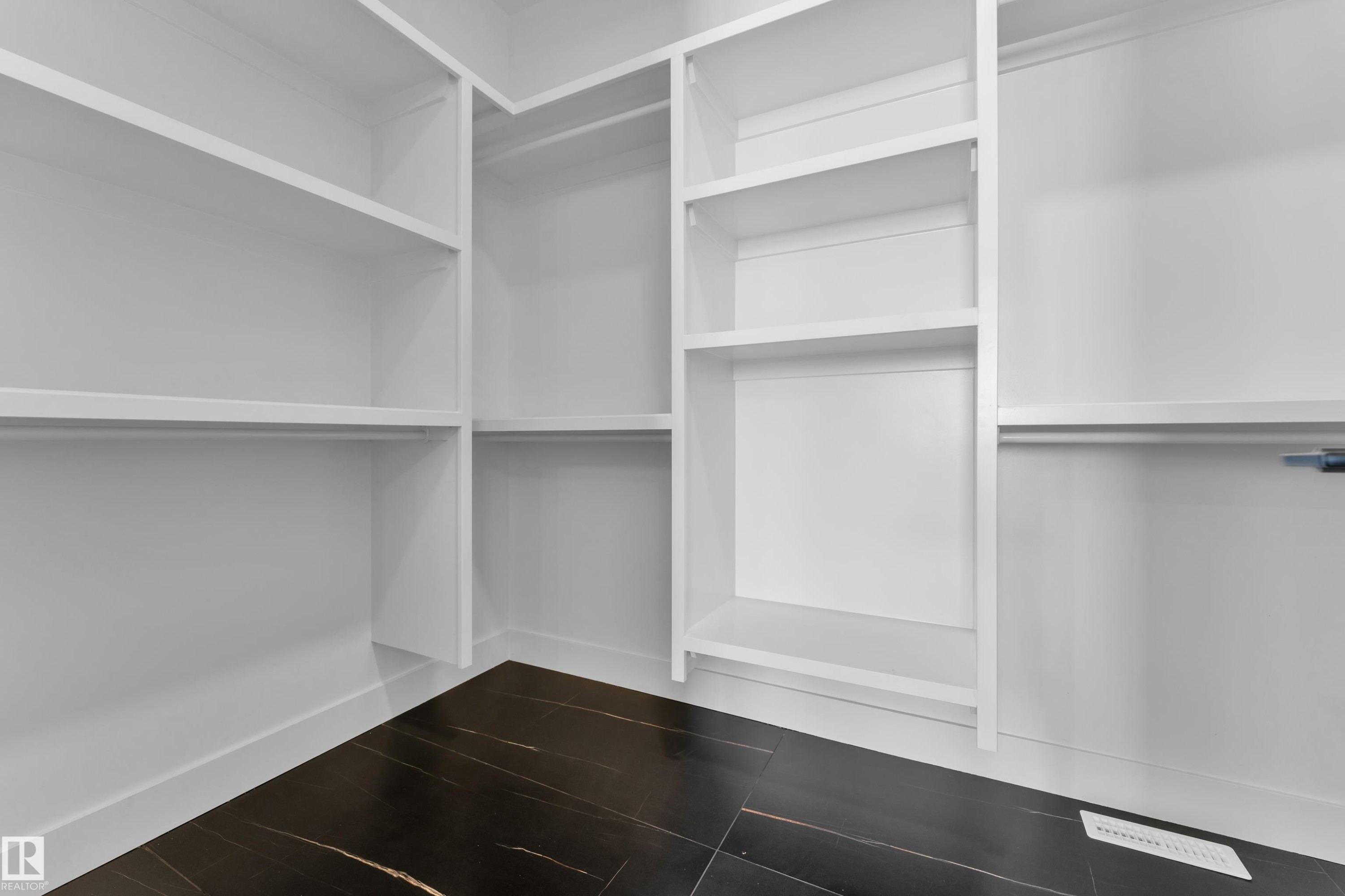 Walk-in closet featuring white built-in shelving, hanging rods, and dark tile flooring - 503 Creekside Bay, Leduc, AB - Indoor With Storage