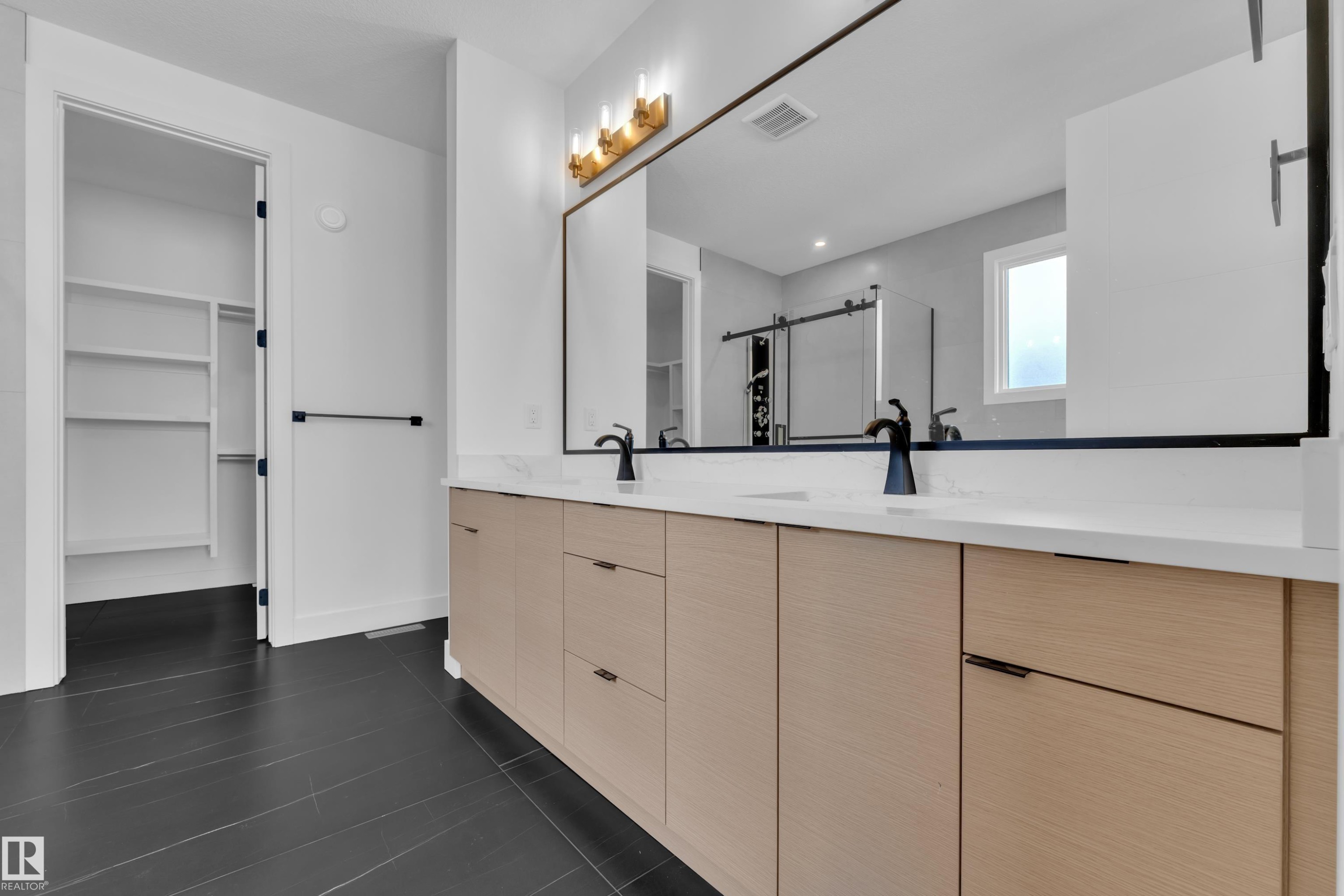 The bathroom features a dual sink vanity with light wood cabinetry, a white countertop, and dark-toned faucets - 503 Creekside Bay, Leduc, AB - Indoor