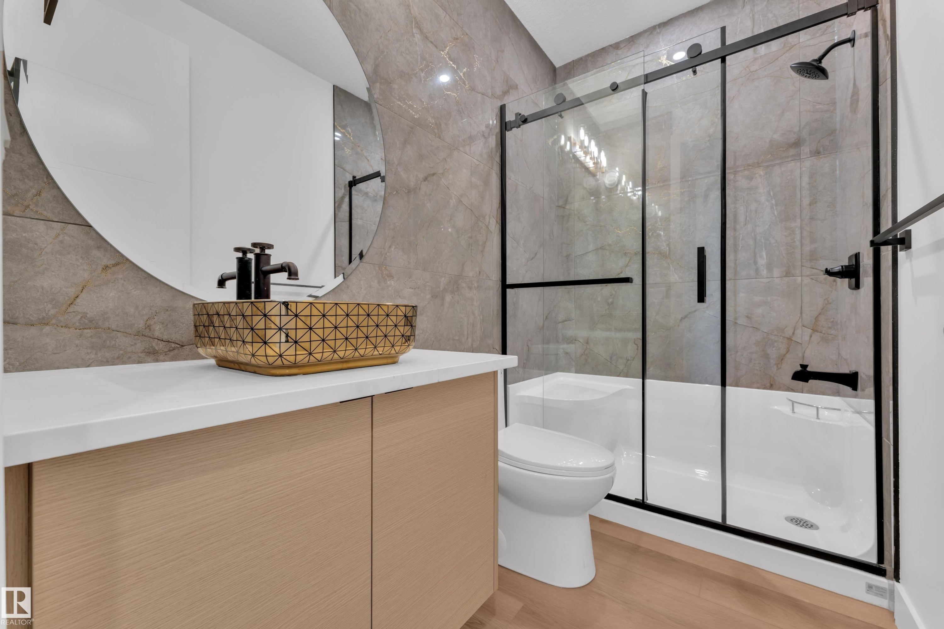 The bathroom features a vessel sink with a geometric pattern, a light wood vanity, and a shower with a sliding glass door and matte black fixtures - 503 Creekside Bay, Leduc, AB - Indoor Photo Showing Bathroom