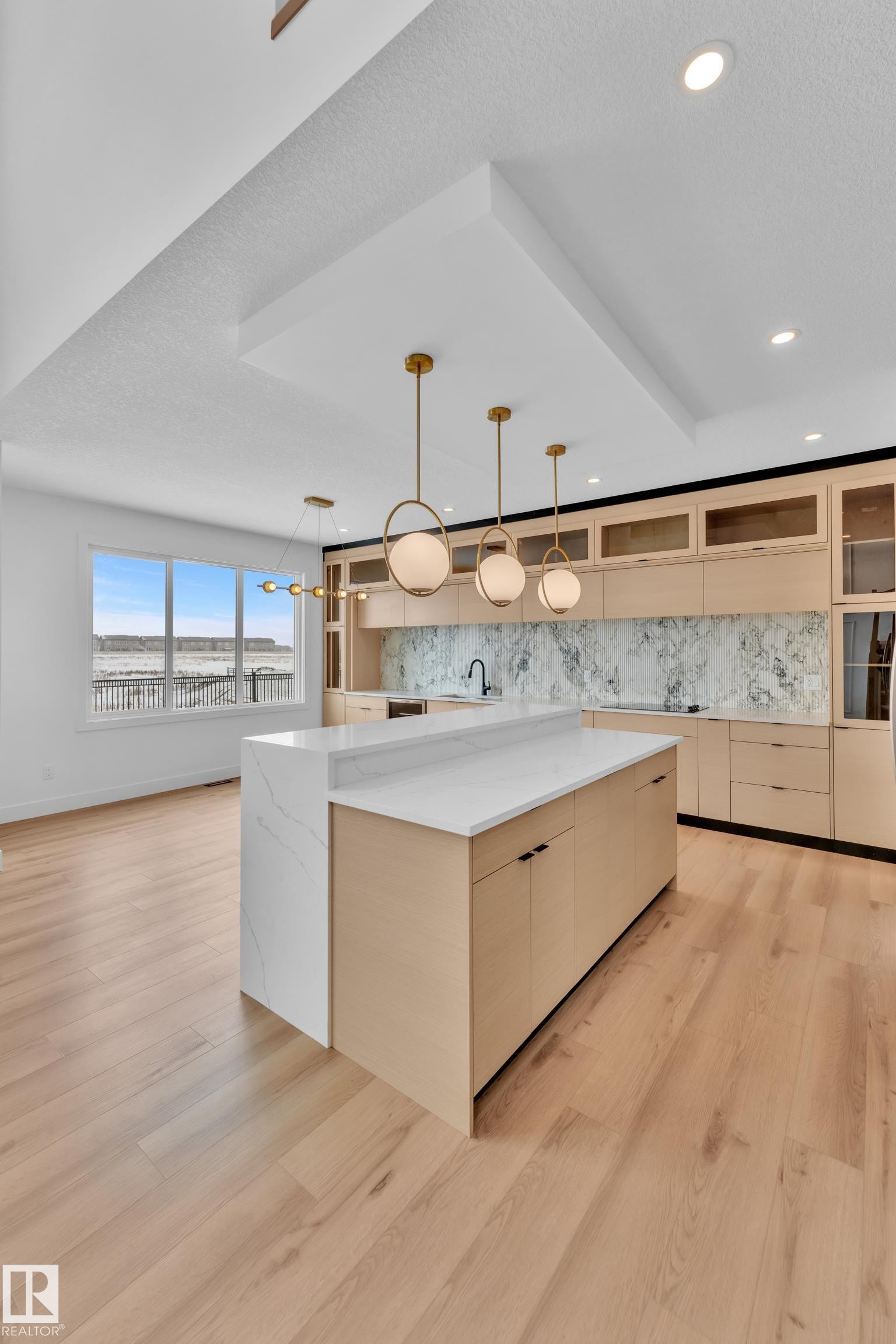 This modern kitchen features light wood flooring, a spacious island with a white countertop, and contemporary pendant lighting - 503 Creekside Bay, Leduc, AB - Indoor Photo Showing Kitchen
