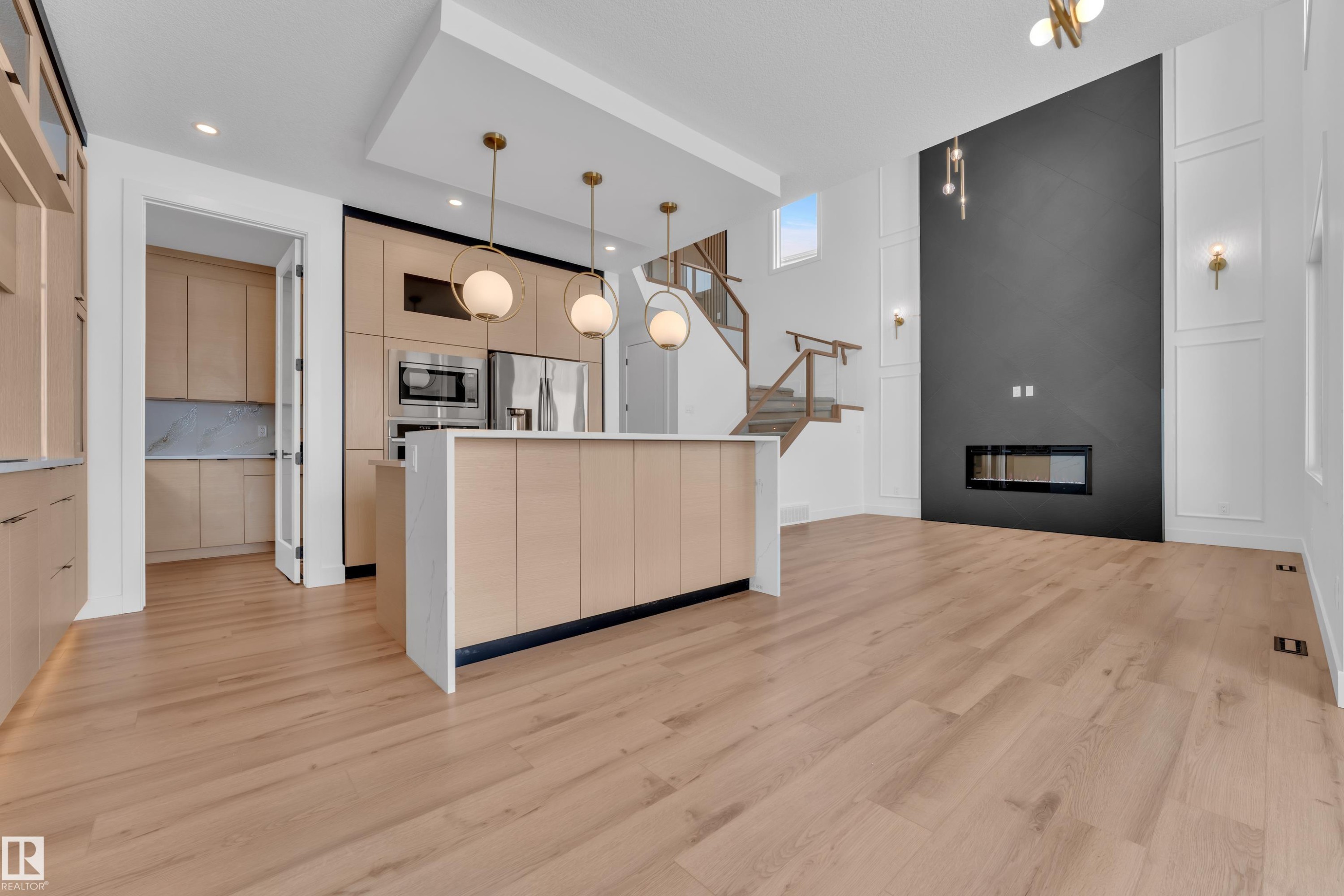 The property features light wood flooring, a kitchen island with pendant lighting, and a modern fireplace integrated into a dark accent wall - 503 Creekside Bay, Leduc, AB - Indoor Photo Showing Kitchen