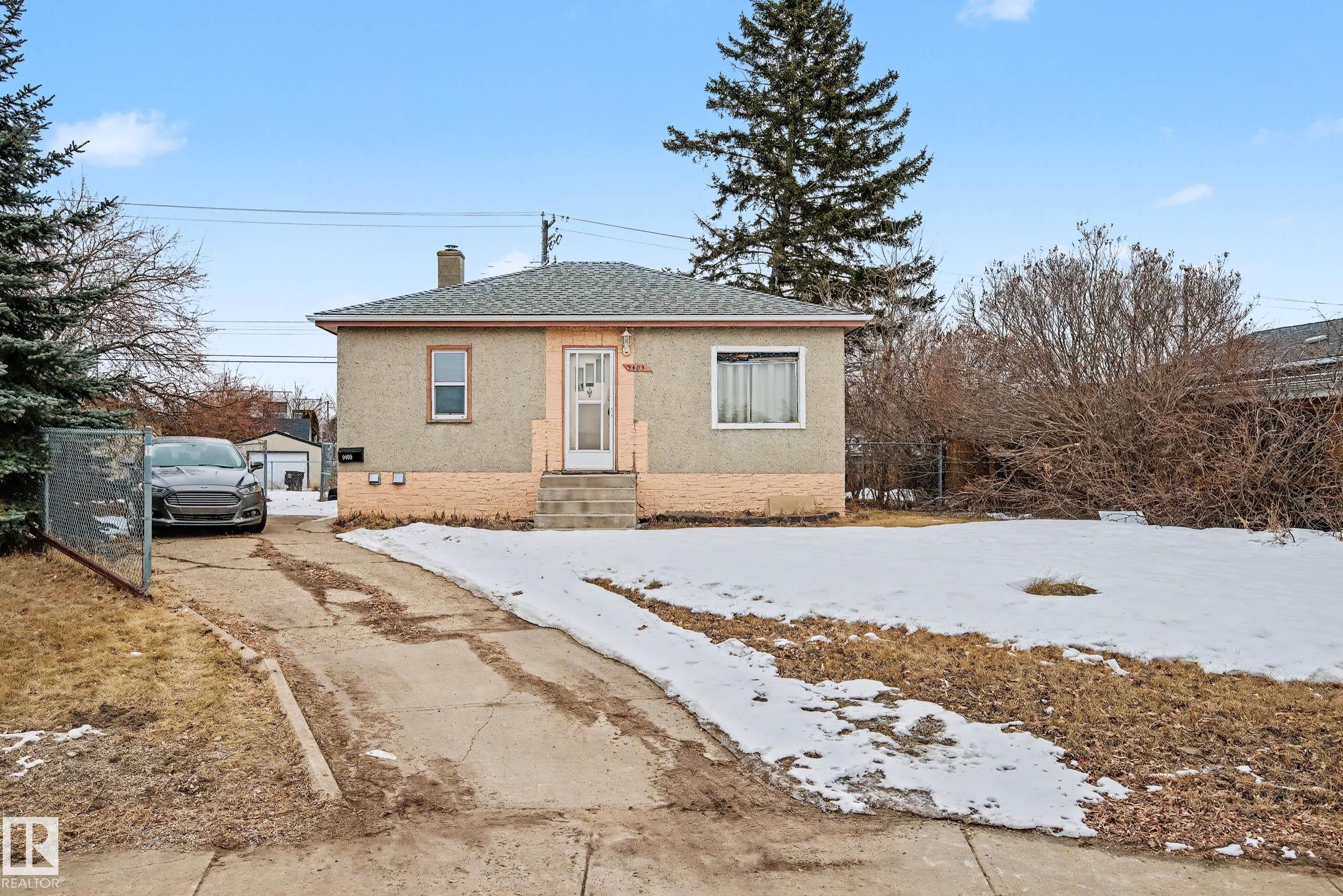 The property features a stucco exterior, a sloped shingled roof, and a front yard with partial snow cover - 9409 154 Street, Edmonton, AB - Outdoor