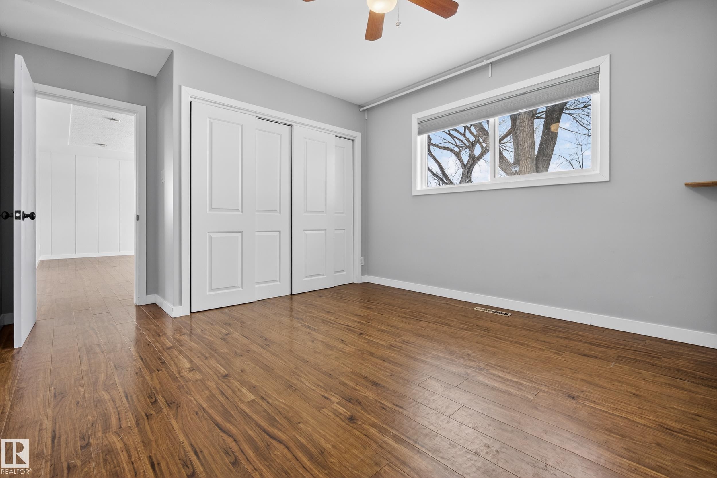 This room features rich wood-look flooring, a window offering exterior views, and white sliding closet doors - 3613 113 Avenue, Edmonton, AB - Indoor Photo Showing Other Room