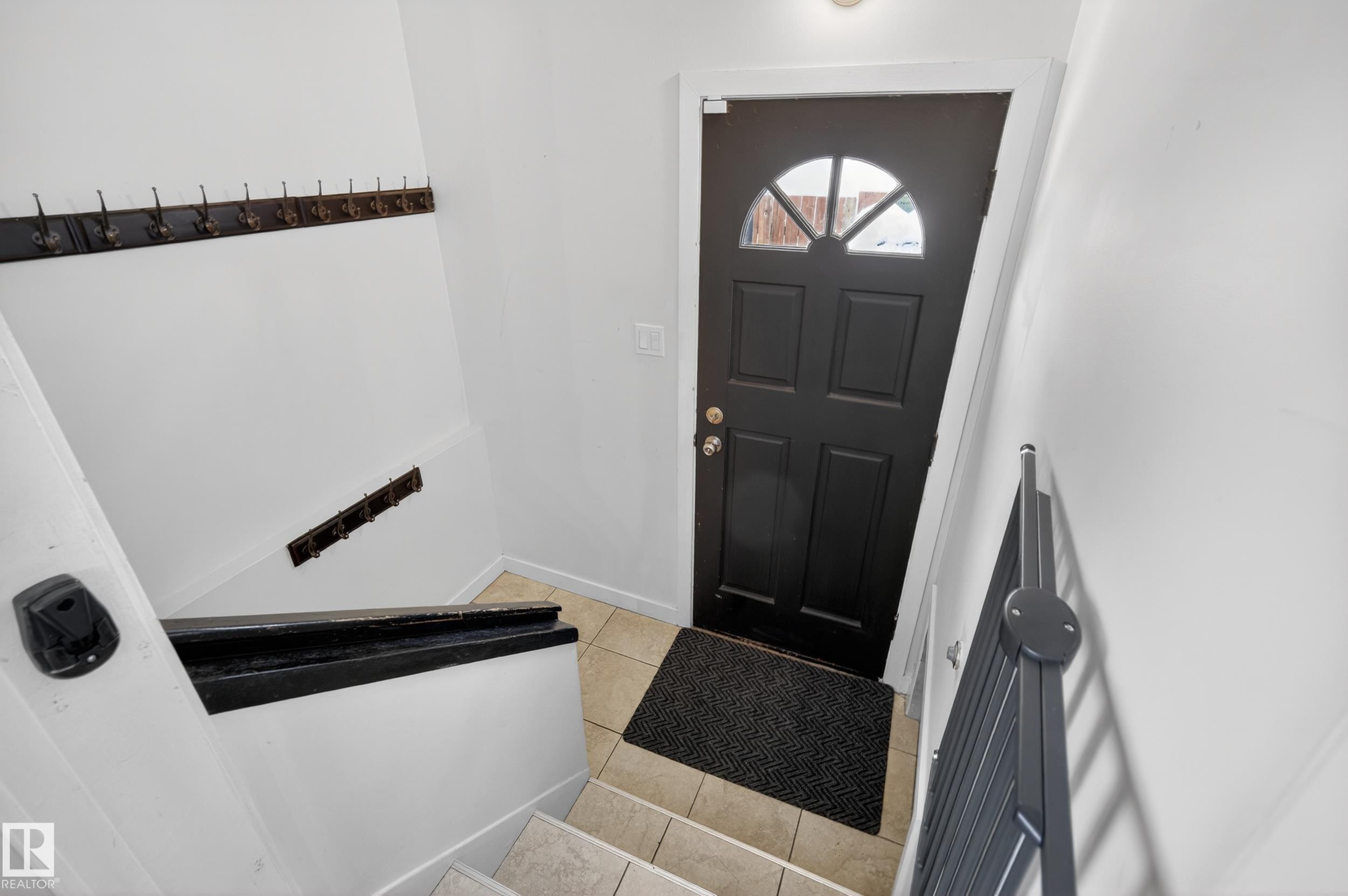 Entryway featuring a black door with an arched window, light tile flooring, and stairs with a black handrail - 3613 113 Avenue, Edmonton, AB - Indoor Photo Showing Other Room
