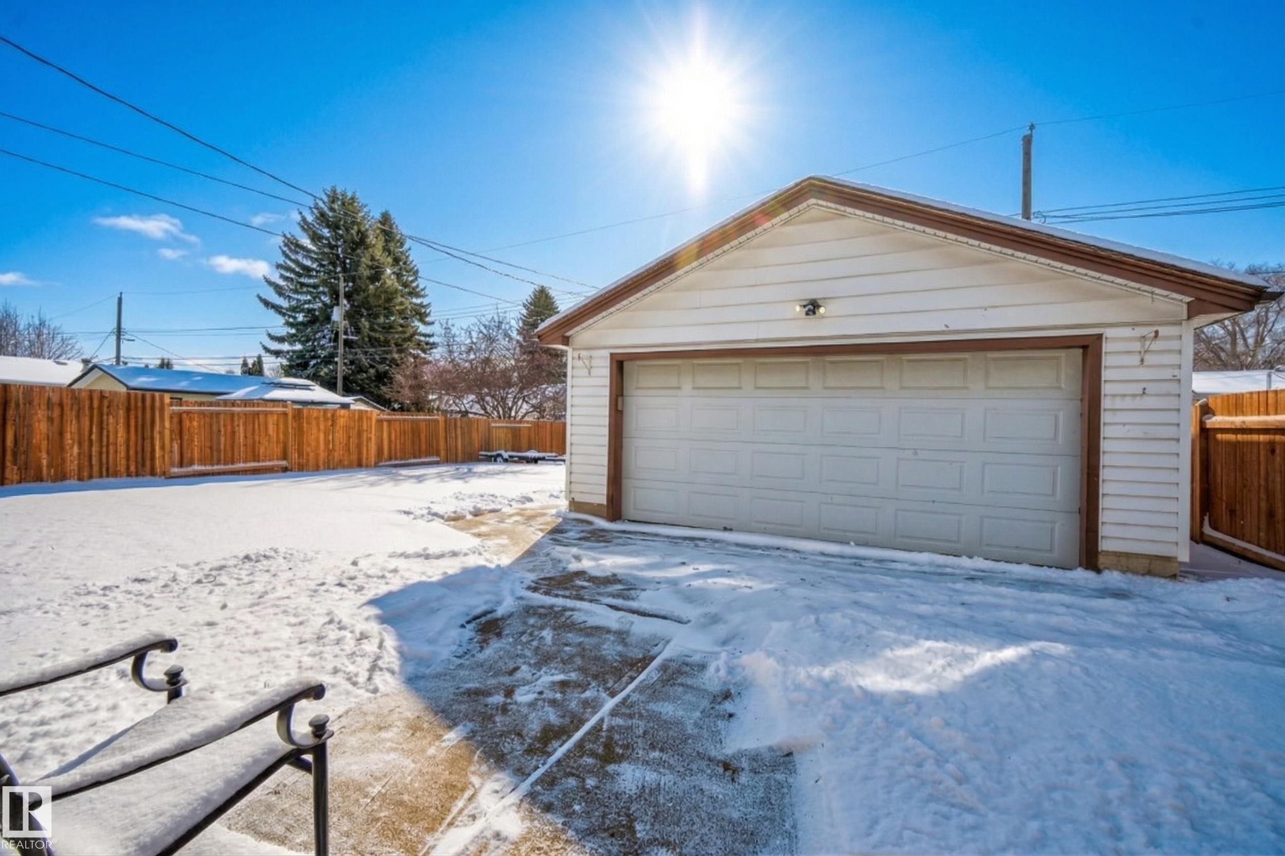 Detached garage with a white garage door, set within a yard enclosed by a wooden fence - 3613 113 Avenue, Edmonton, AB - Outdoor