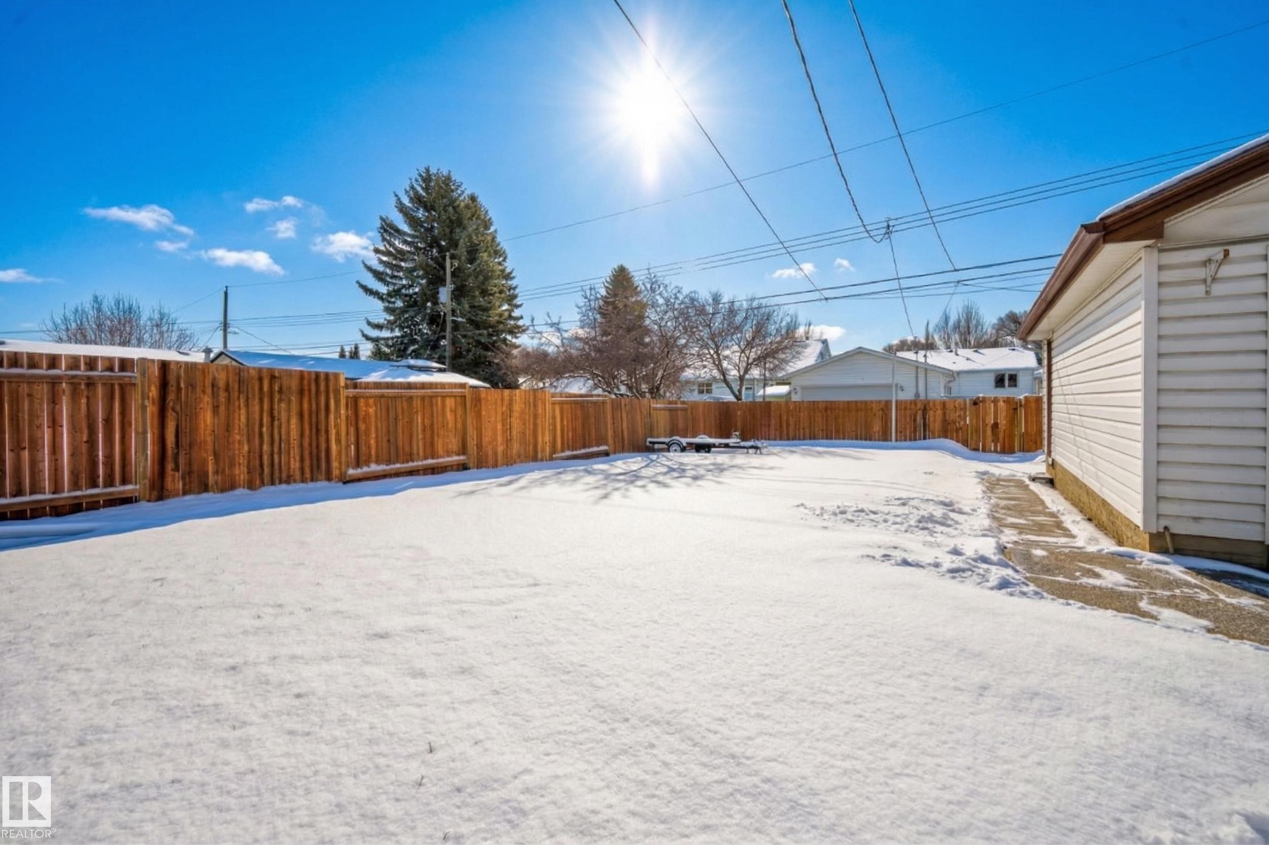 The property features a spacious yard with a wood fence and a visible section of the home's exterior siding - 3613 113 Avenue, Edmonton, AB - Outdoor