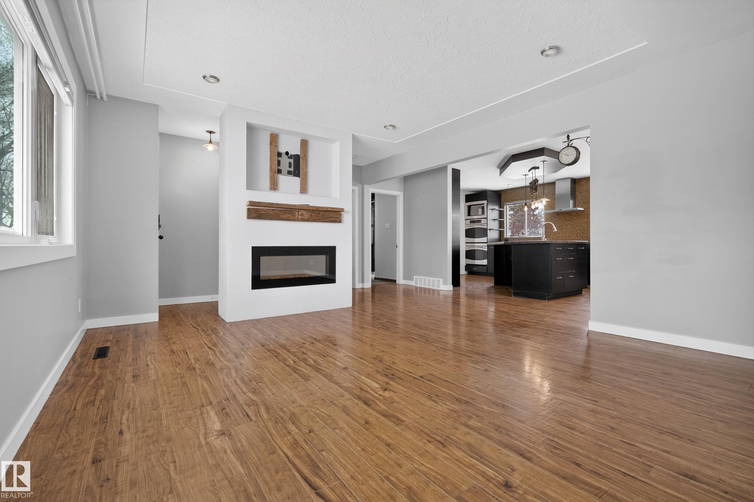 This property features hardwood flooring throughout, a contemporary fireplace with a rustic wood mantel, and large windows providing natural light - 3613 113 Avenue, Edmonton, AB - Indoor Photo Showing Living Room With Fireplace