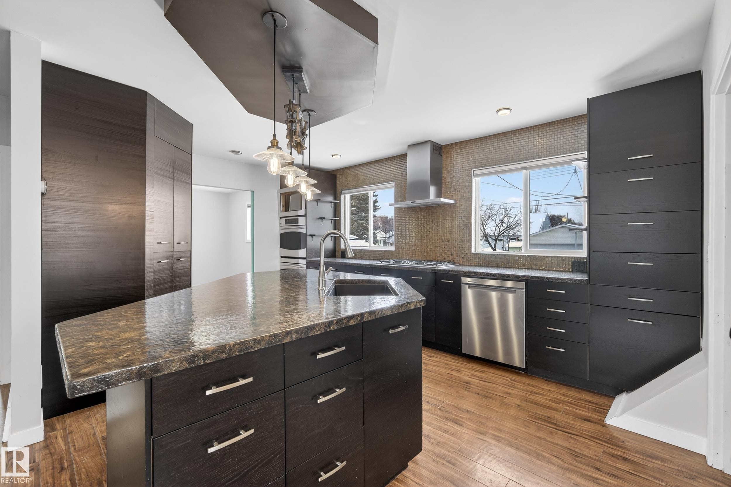 The kitchen features dark cabinetry, a large kitchen island with a stone countertop, and stainless steel appliances - 3613 113 Avenue, Edmonton, AB - Indoor Photo Showing Kitchen With Upgraded Kitchen