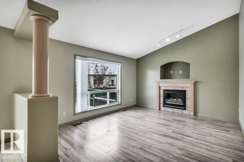 Living area featuring an angled vaulted ceiling, a large window, and a fireplace with a mantel and an arched alcove - 902 Graham Wynd, Edmonton, AB - Indoor Photo Showing Living Room With Fireplace