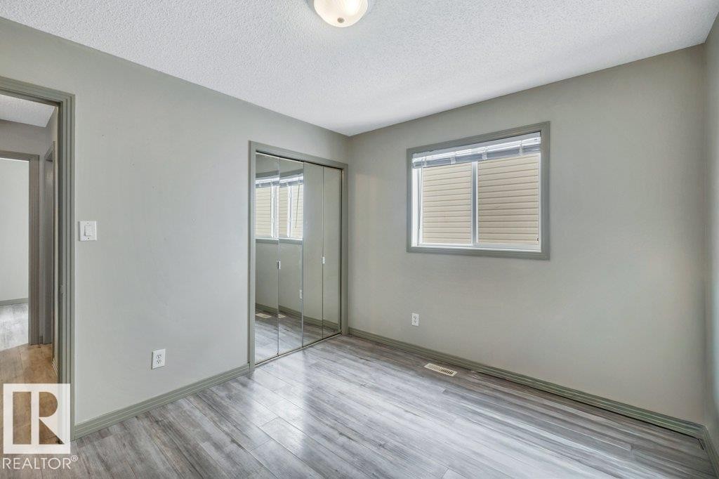 This room features grey walls, wood-look flooring, a window with horizontal blinds, and a mirrored closet - 902 Graham Wynd, Edmonton, AB - Indoor Photo Showing Other Room