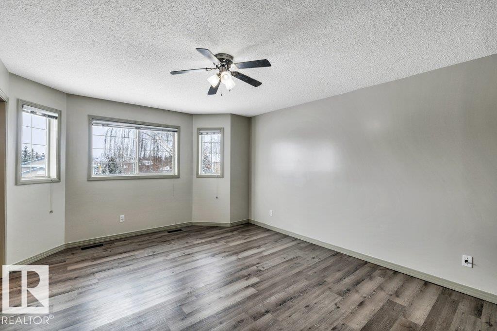 Spacious room featuring wood-style flooring, a ceiling fan with light fixture, and multiple windows providing views of the outdoors - 902 Graham Wynd, Edmonton, AB - Indoor Photo Showing Other Room