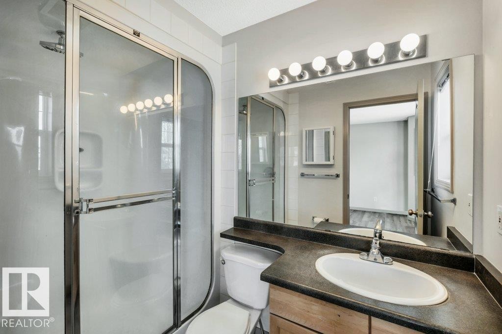 Bathroom featuring a shower with a sliding glass door, a vanity with a dark countertop and an oval sink, and a large mirror with overhead lighting - 902 Graham Wynd, Edmonton, AB - Indoor Photo Showing Bathroom