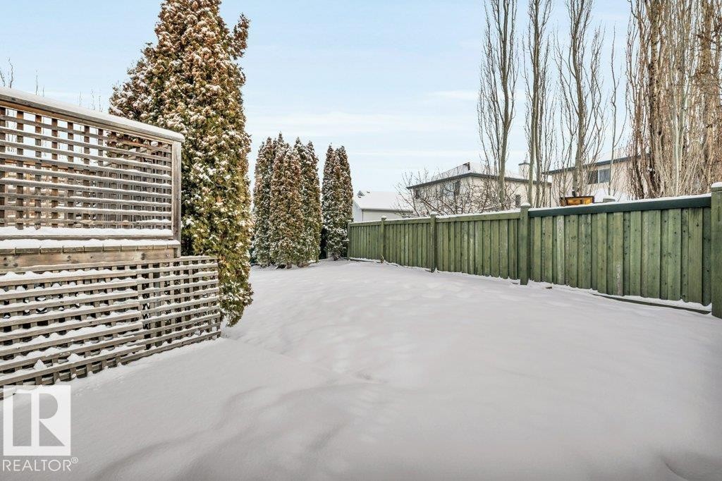 The property features a large yard with a green wooden fence and tall evergreen trees - 902 Graham Wynd, Edmonton, AB - Outdoor