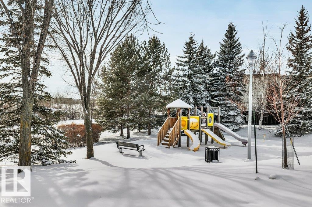 The property is located in a community with a playground featuring slides and climbing structures, surrounded by snow-covered evergreen trees and a park bench - 902 Graham Wynd, Edmonton, AB - Outdoor