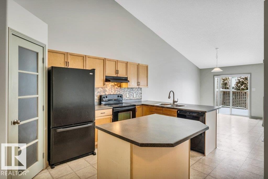 The kitchen features light wood cabinetry, a tiled backsplash, and a central island with a countertop - 902 Graham Wynd, Edmonton, AB - Indoor Photo Showing Kitchen With Double Sink
