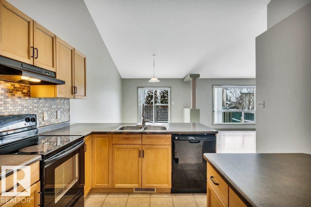 The kitchen features light wood cabinetry, black appliances including a stove and dishwasher, and a double basin sink - 902 Graham Wynd, Edmonton, AB - Indoor Photo Showing Kitchen With Double Sink