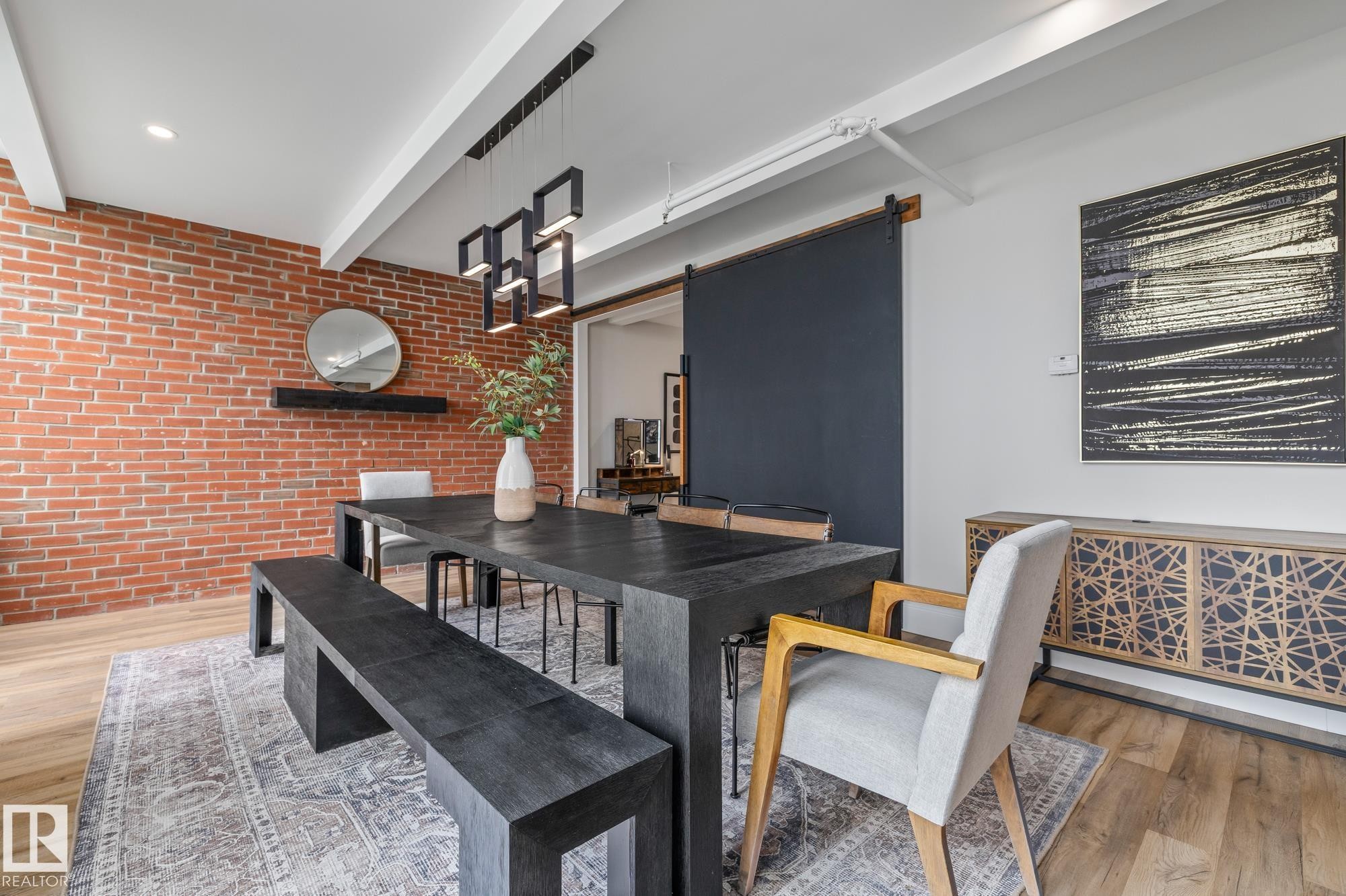 Dining area featuring a red brick accent wall, light hardwood floors, and a dark sliding barn door - 314 10309 107 Street, Edmonton, AB -