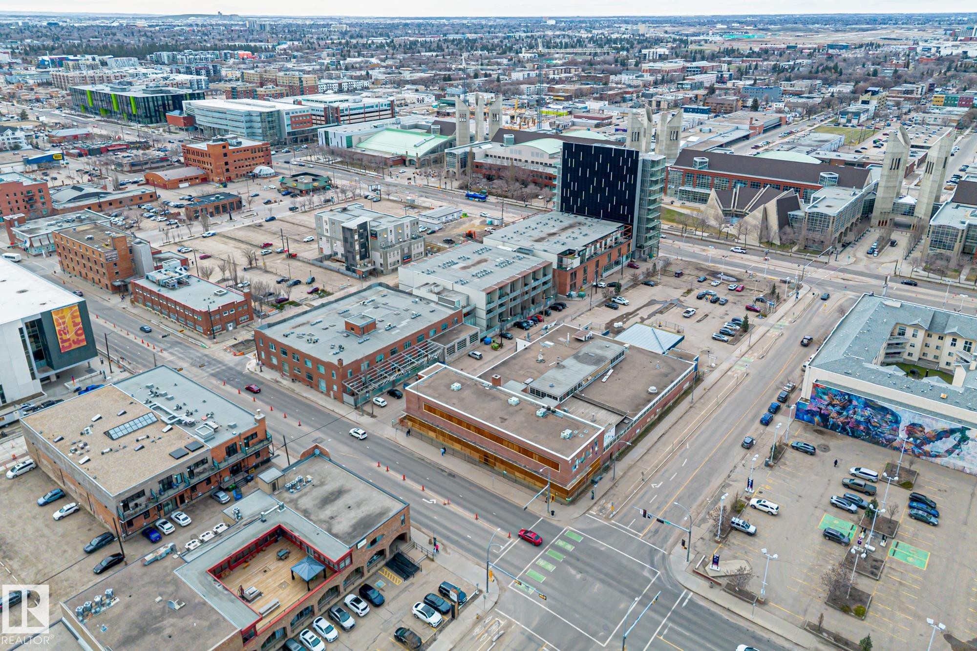 Aerial view of the neighborhood showcasing various commercial and residential buildings, paved roads, and several parking areas - 314 10309 107 Street, Edmonton, AB - With View