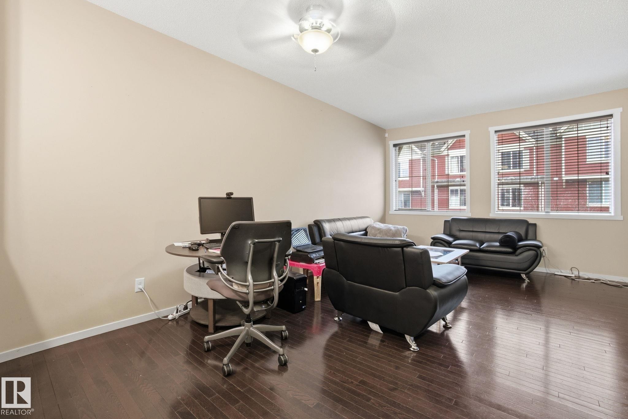 Living area featuring dark hardwood floors, two windows with blinds, and a ceiling fan - 75 603 Watt Boulevard, Edmonton, AB - Indoor