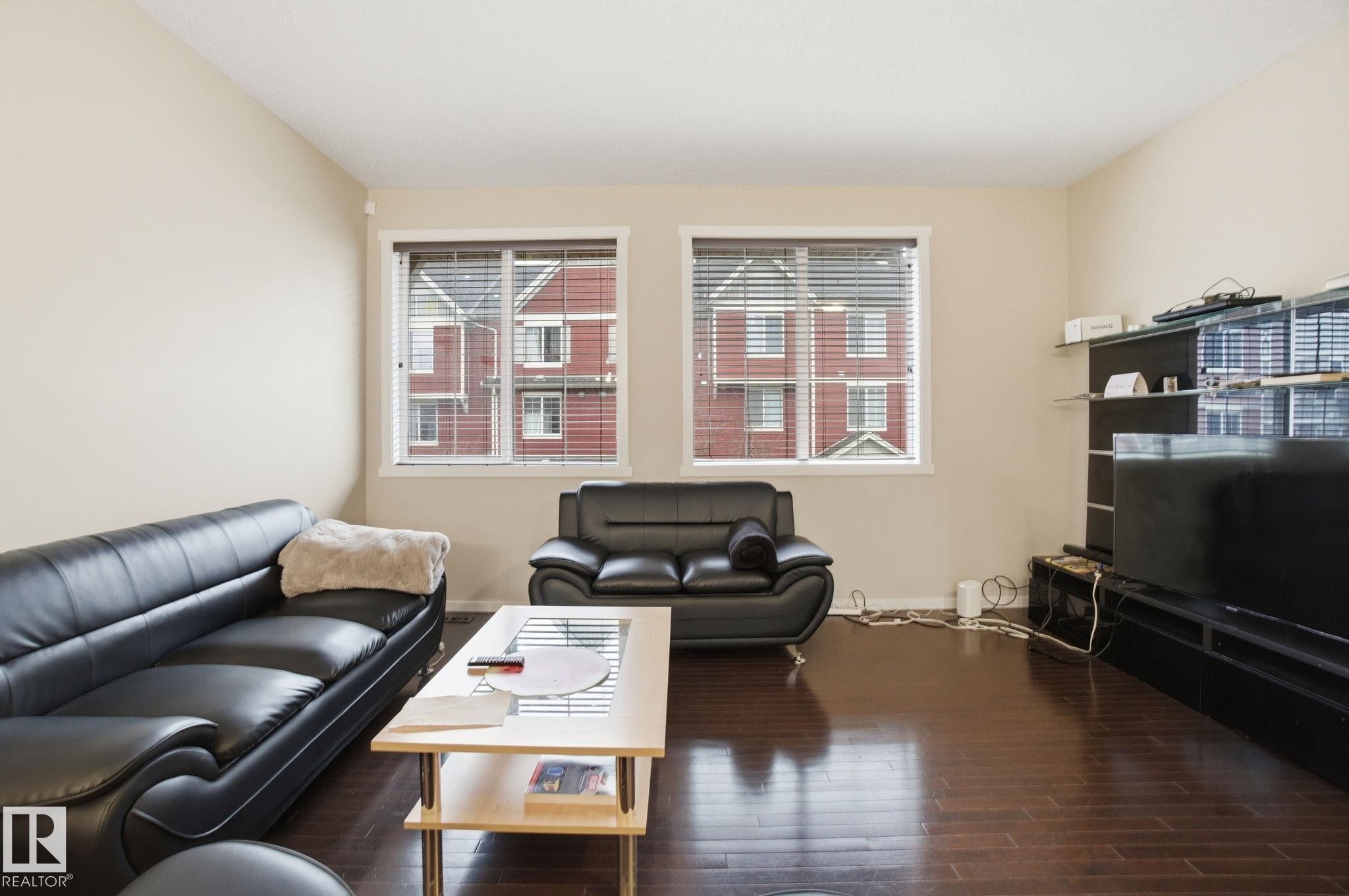 Living area featuring dark hardwood floors, light neutral walls, and two windows with white blinds - 75 603 Watt Boulevard, Edmonton, AB - Indoor Photo Showing Living Room