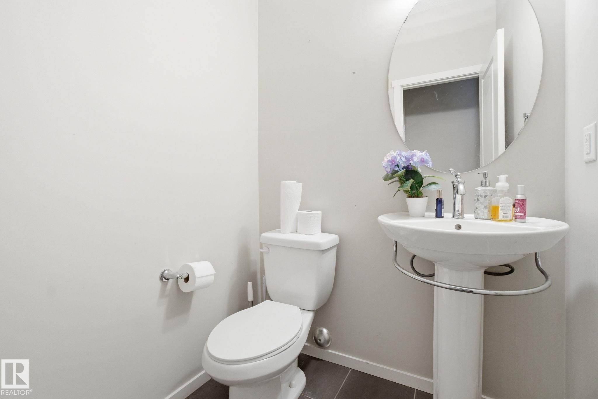 Bathroom featuring a pedestal sink, a circular mirror, and a toilet - 75 603 Watt Boulevard, Edmonton, AB - Indoor Photo Showing Bathroom