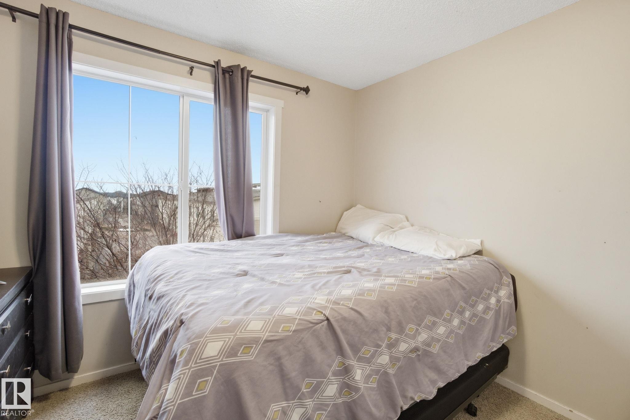 The room features a window with a view of the surrounding neighborhood, neutral wall paint, and carpeted flooring - 75 603 Watt Boulevard, Edmonton, AB - Indoor Photo Showing Bedroom