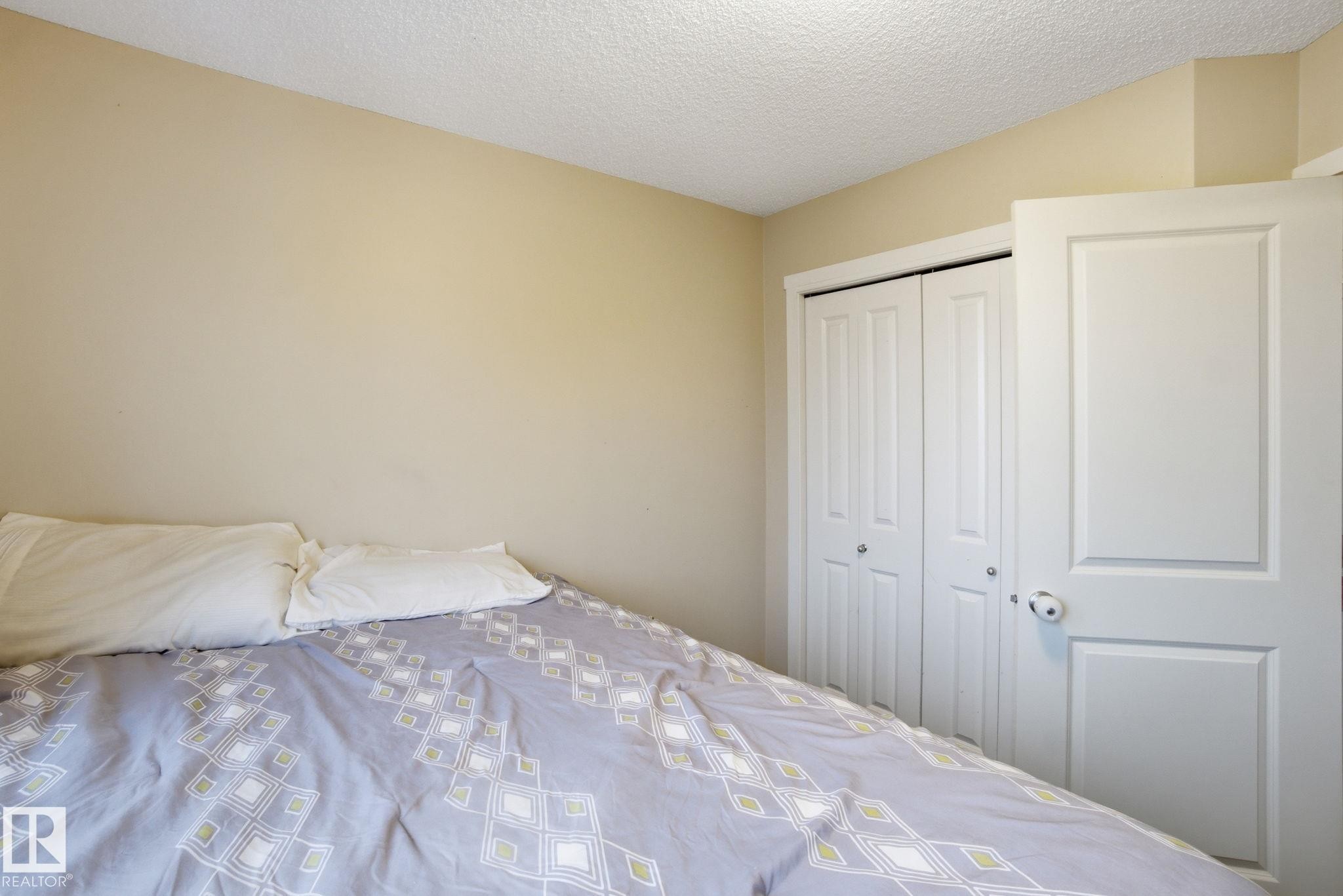 Room with light-colored walls and a textured ceiling, featuring a white bi-fold closet door and a white panel door - 75 603 Watt Boulevard, Edmonton, AB - Indoor Photo Showing Bedroom
