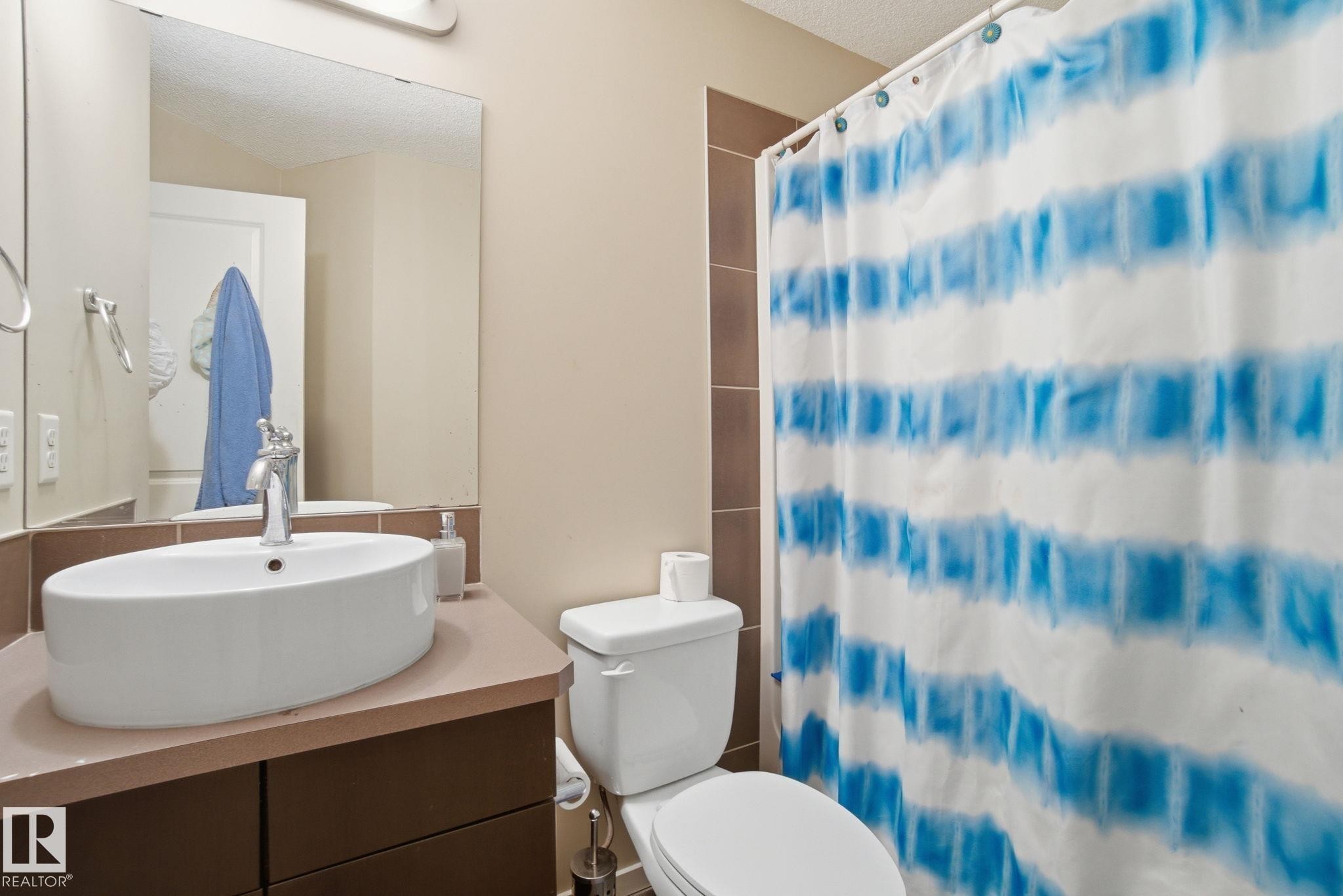 This bathroom features a contemporary vessel sink, a vanity with a counter, and a toilet - 75 603 Watt Boulevard, Edmonton, AB - Indoor Photo Showing Bathroom