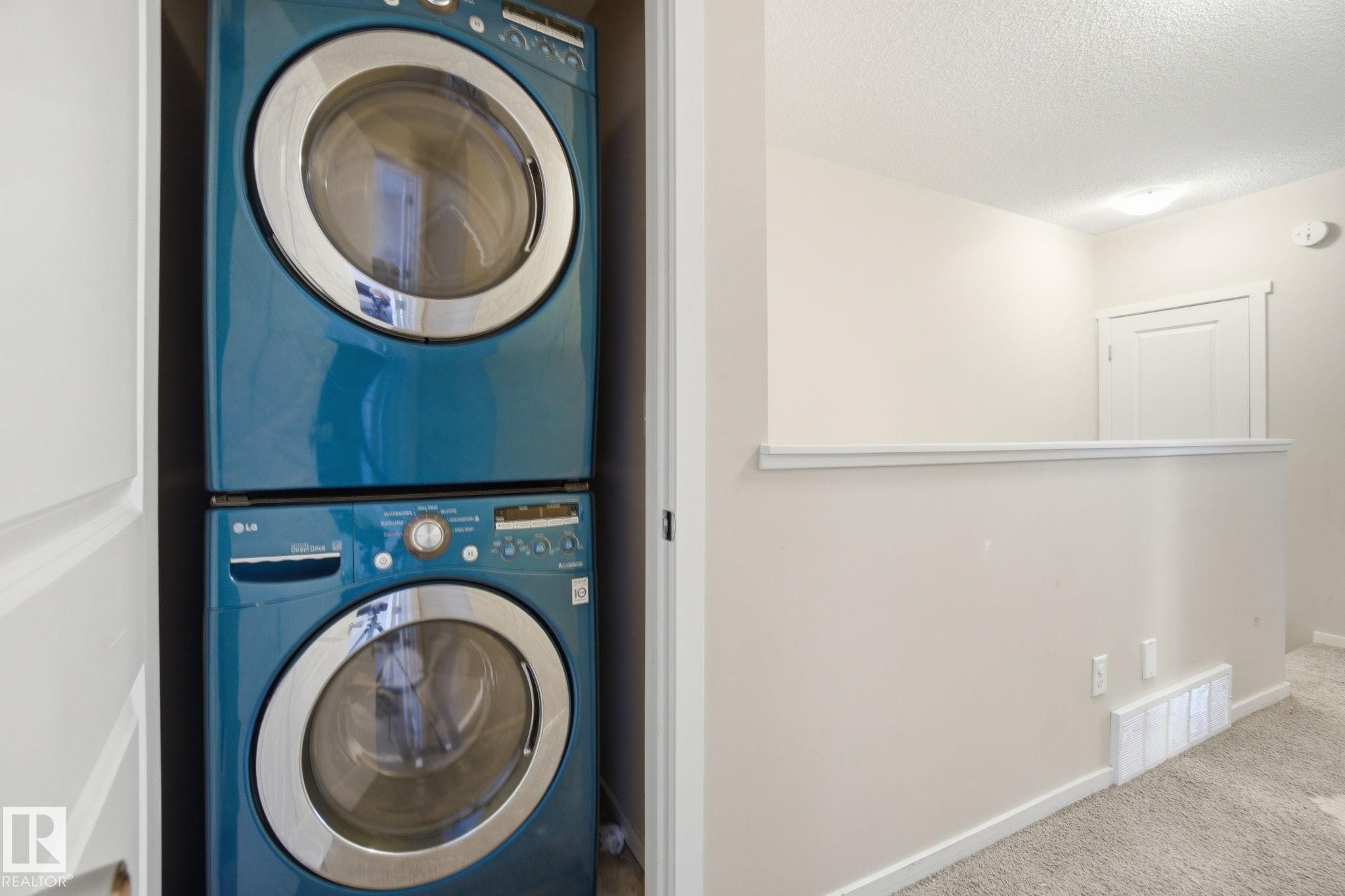Conveniently located laundry area featuring a stacked washer and dryer set, with a light-colored wall and carpeted flooring - 75 603 Watt Boulevard, Edmonton, AB - Indoor Photo Showing Laundry Room