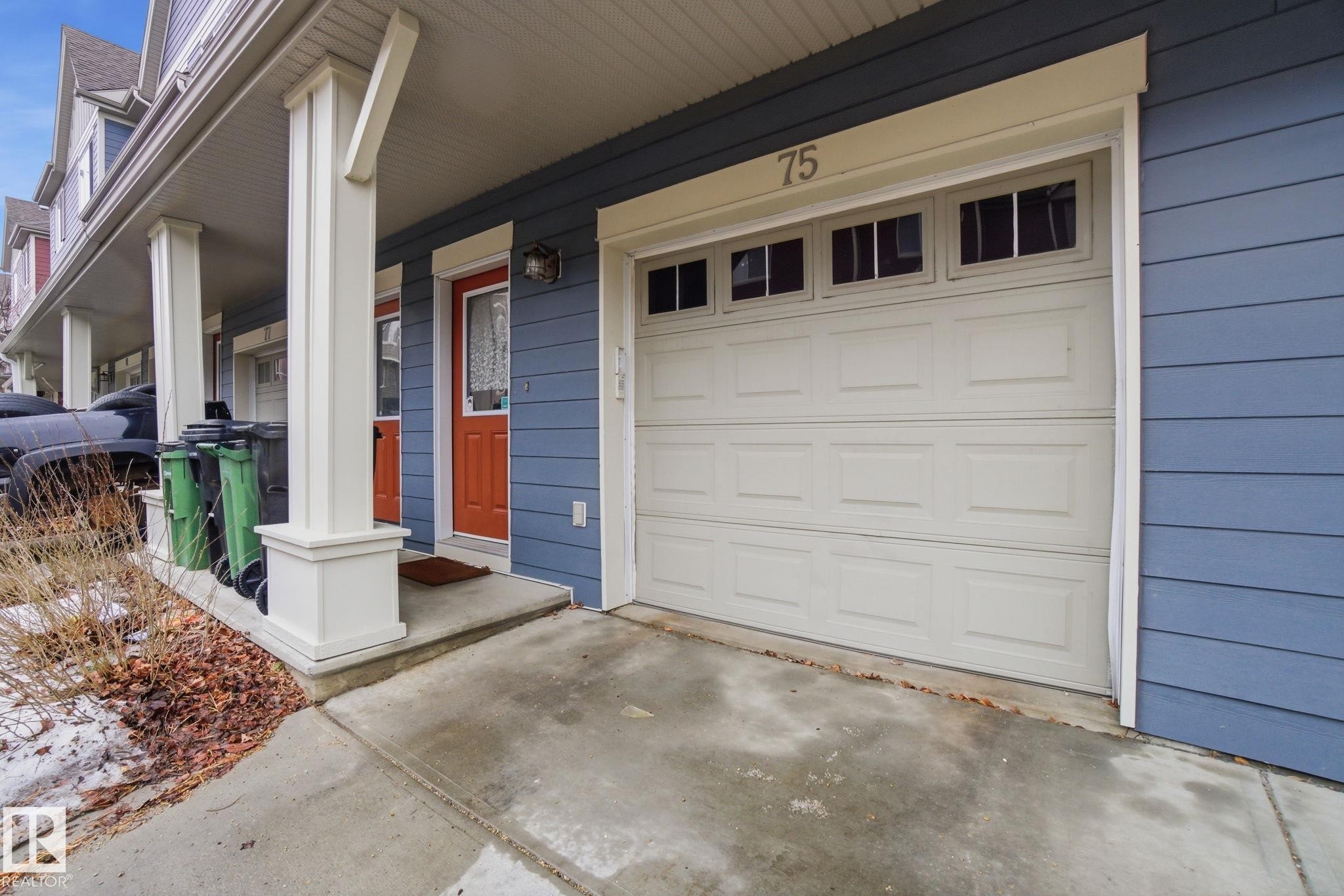 The property features blue siding, a white garage door with windows, and a front entry with an orange door - 75 603 Watt Boulevard, Edmonton, AB - Outdoor With Exterior