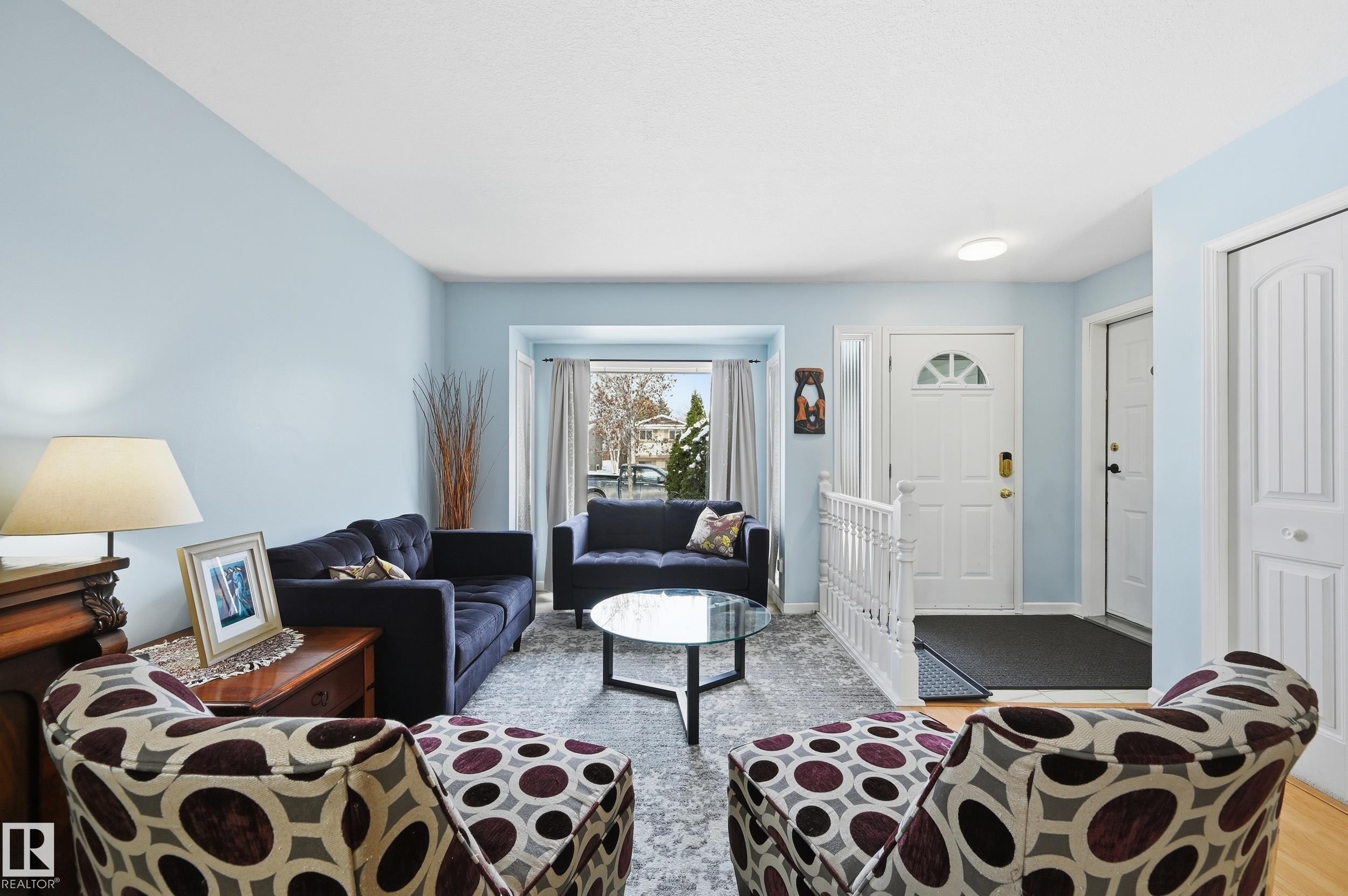 Living area featuring light blue walls, a white front door with a half-moon window, and a bay window providing natural light - 85 Arlington Drive, St. Albert, AB - Indoor