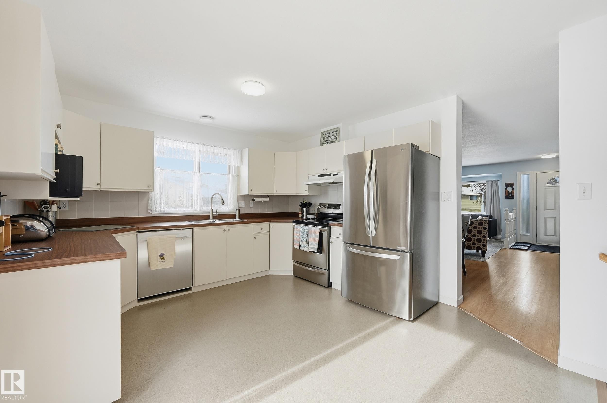 The kitchen features light-colored cabinetry, a window with a sheer curtain, and stainless steel appliances including a refrigerator, dishwasher, and range with an overhead microwave - 85 Arlington Drive, St. Albert, AB - Indoor Photo Showing Kitchen