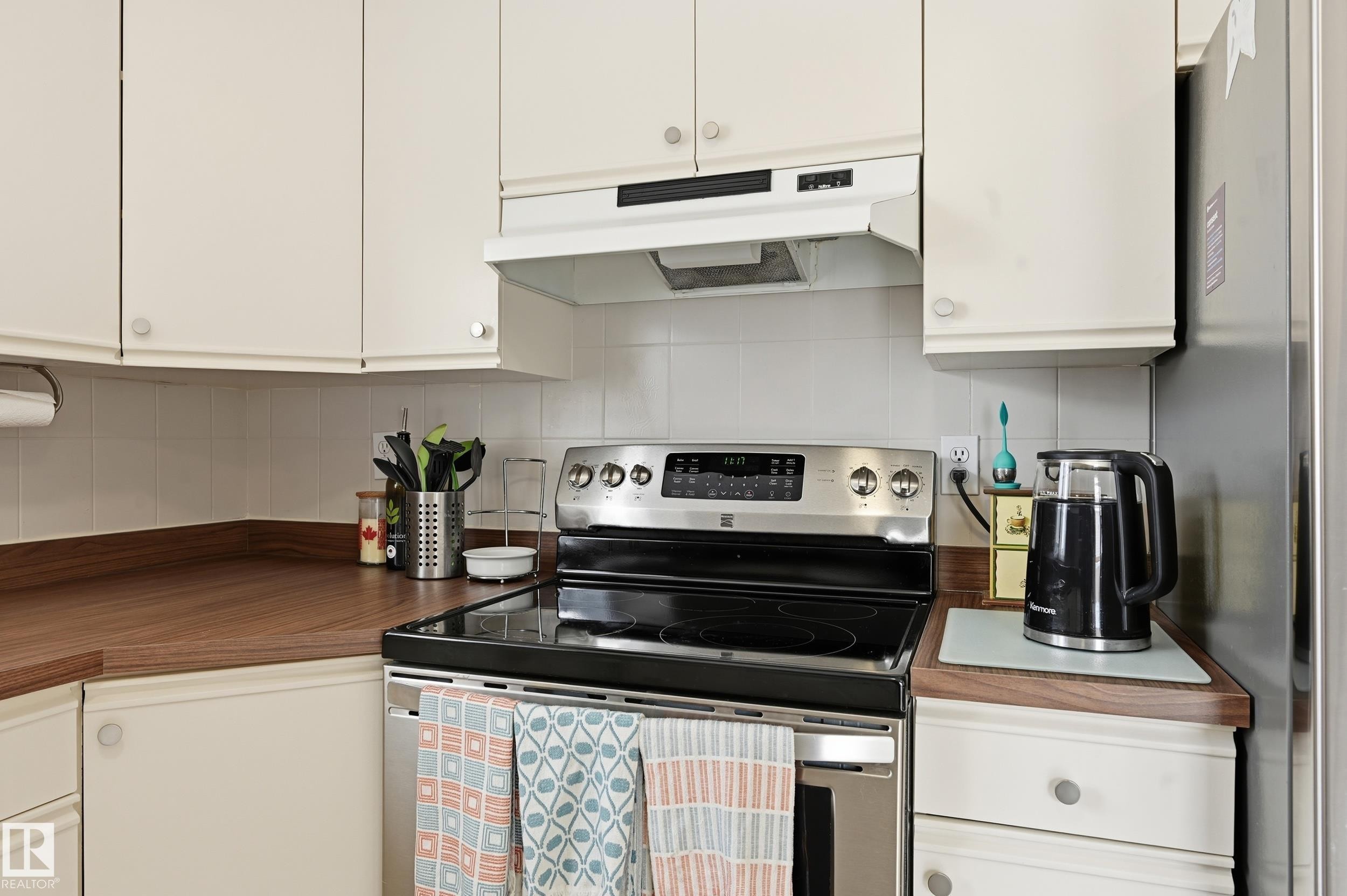 The kitchen features white cabinetry, wooden countertops, a white tiled backsplash, and a stainless steel electric stove with an overhead range hood - 85 Arlington Drive, St. Albert, AB - Indoor Photo Showing Kitchen
