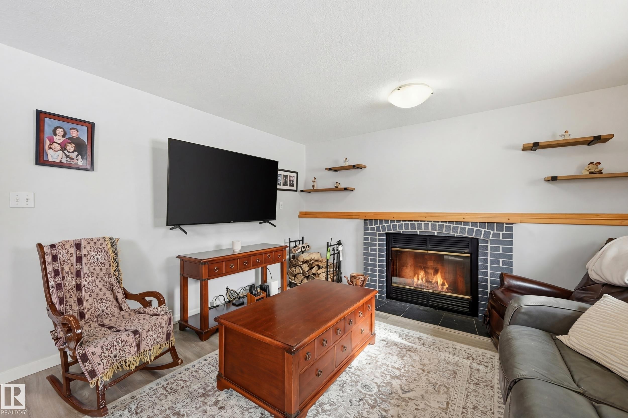 Living area featuring a fireplace with a grey brick surround, light wood flooring, and light wall paint - 85 Arlington Drive, St. Albert, AB - Indoor Photo Showing Living Room With Fireplace