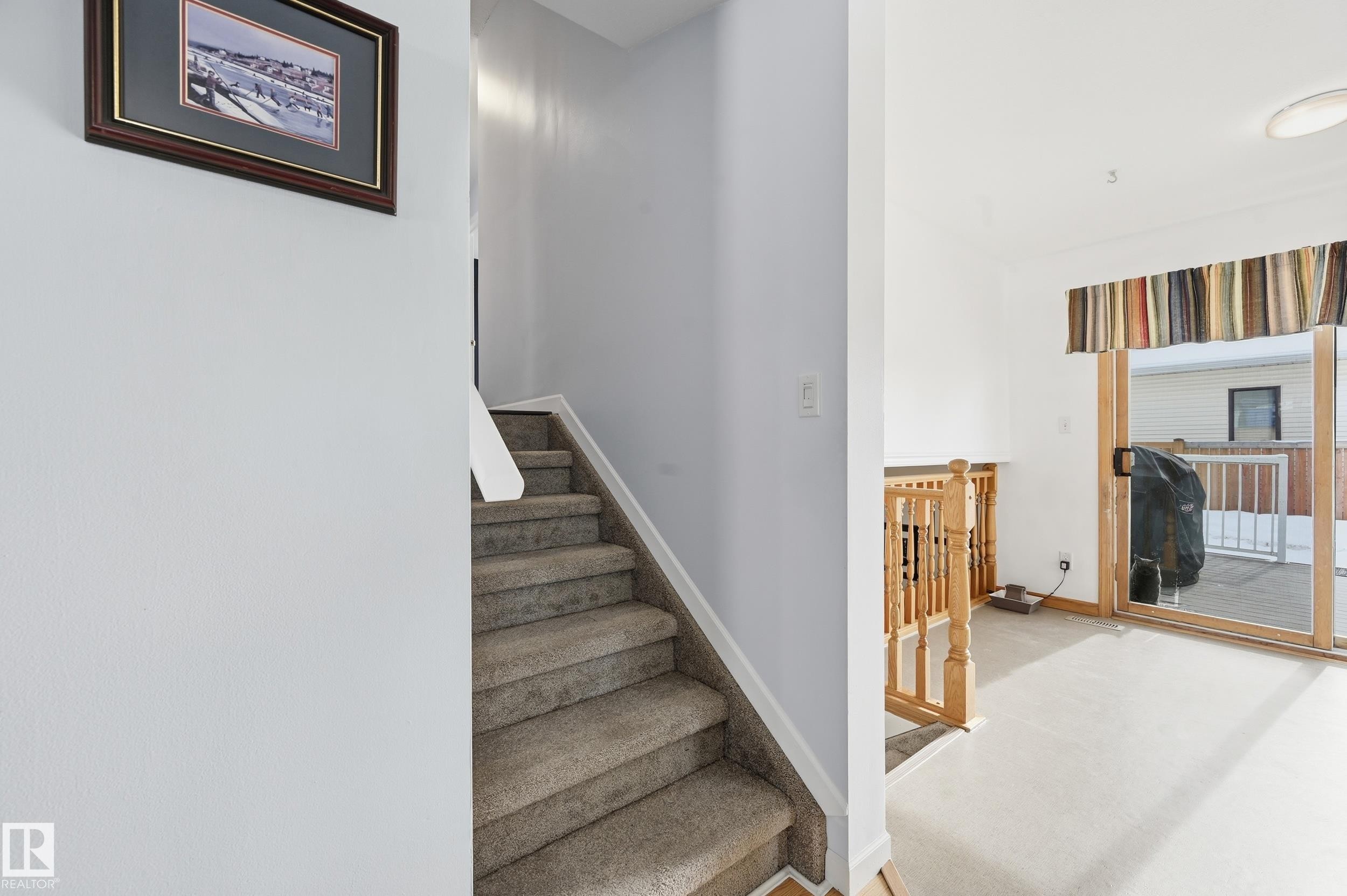 The property features a staircase with carpeted treads and a wooden railing, alongside a room with a sliding glass door leading to an outdoor deck - 85 Arlington Drive, St. Albert, AB - Indoor Photo Showing Other Room