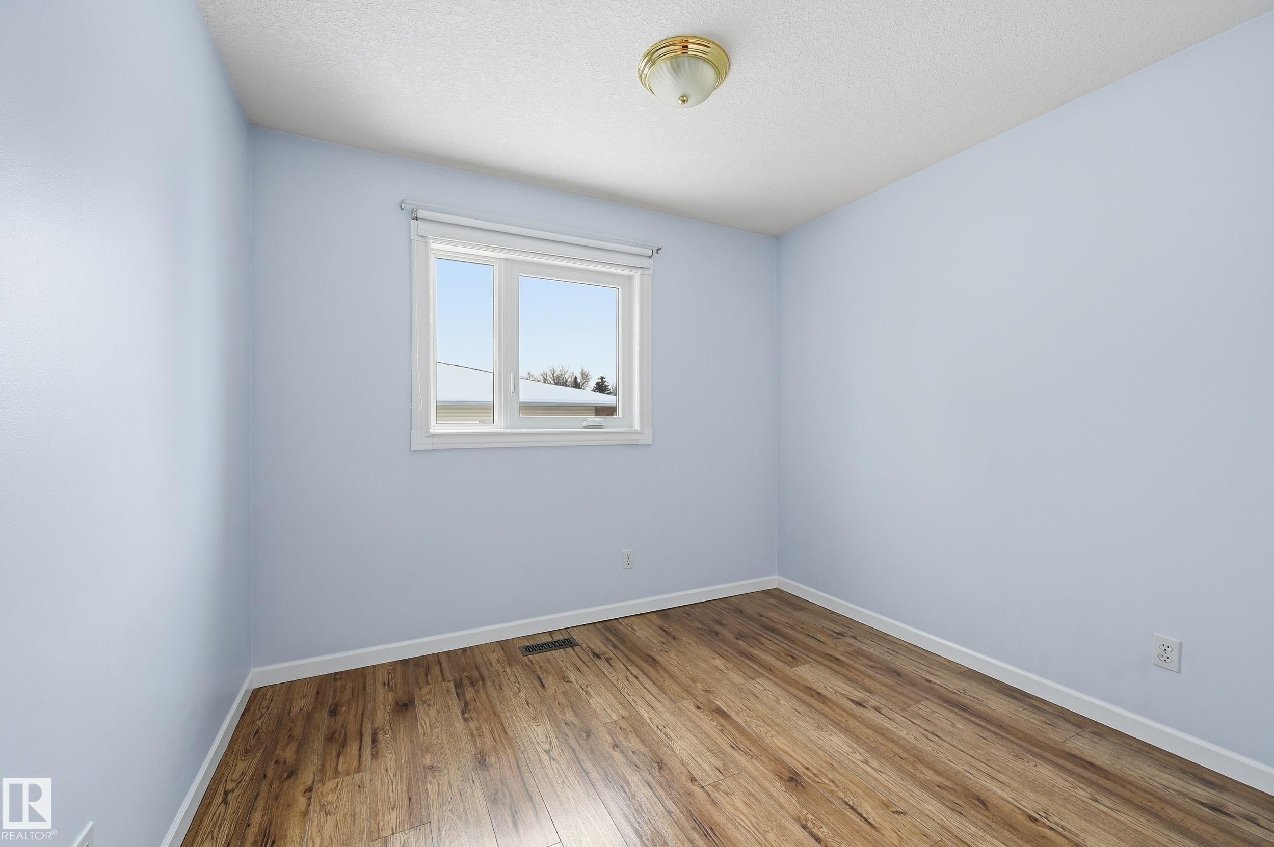 The room features light blue walls, wood-style flooring, a window providing natural light, and a ceiling light fixture - 85 Arlington Drive, St. Albert, AB - Indoor Photo Showing Other Room