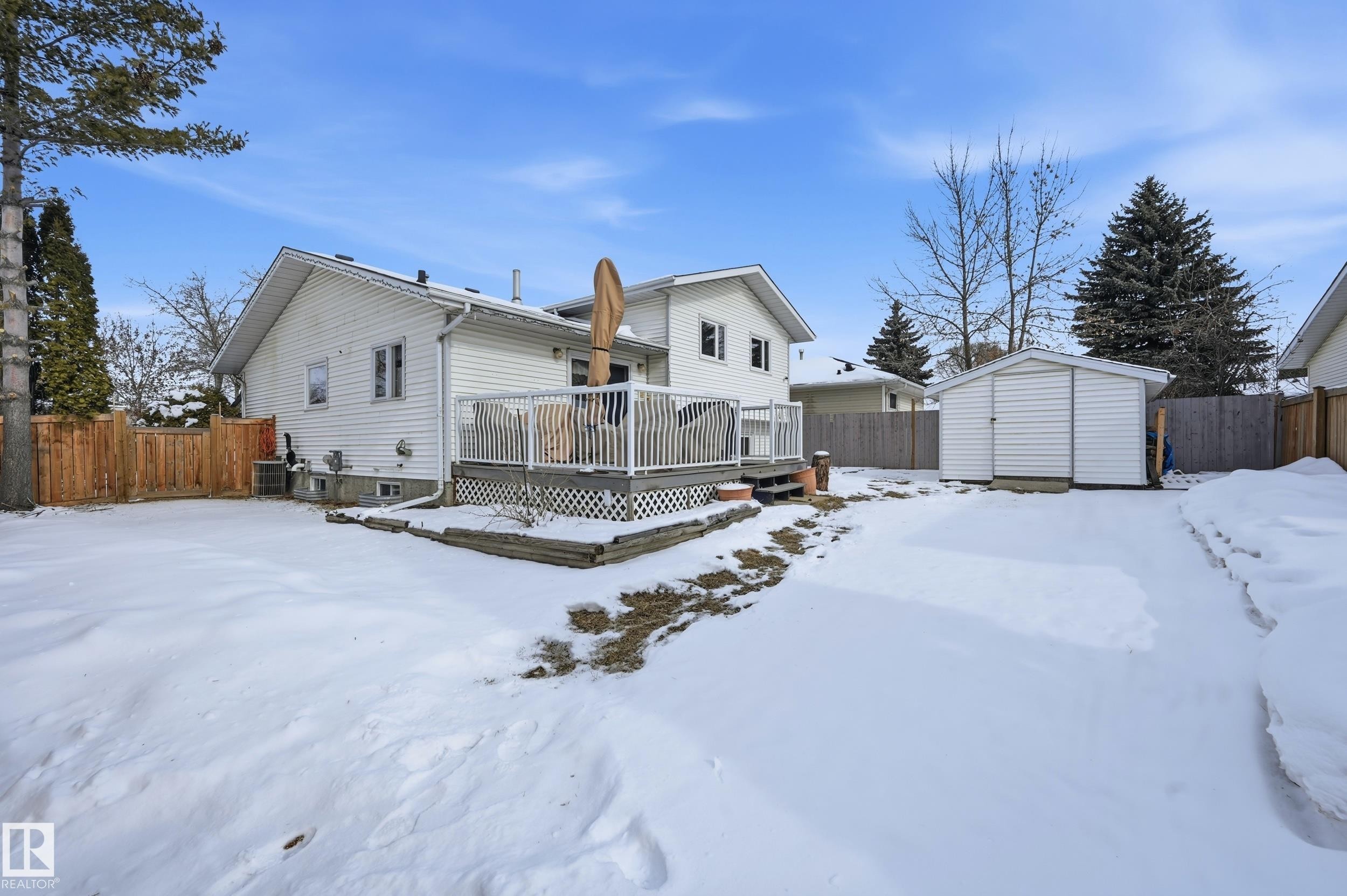 The property features a spacious yard with a white-sided shed, a wooden fence, and mature trees - 85 Arlington Drive, St. Albert, AB - Outdoor With Deck Patio Veranda