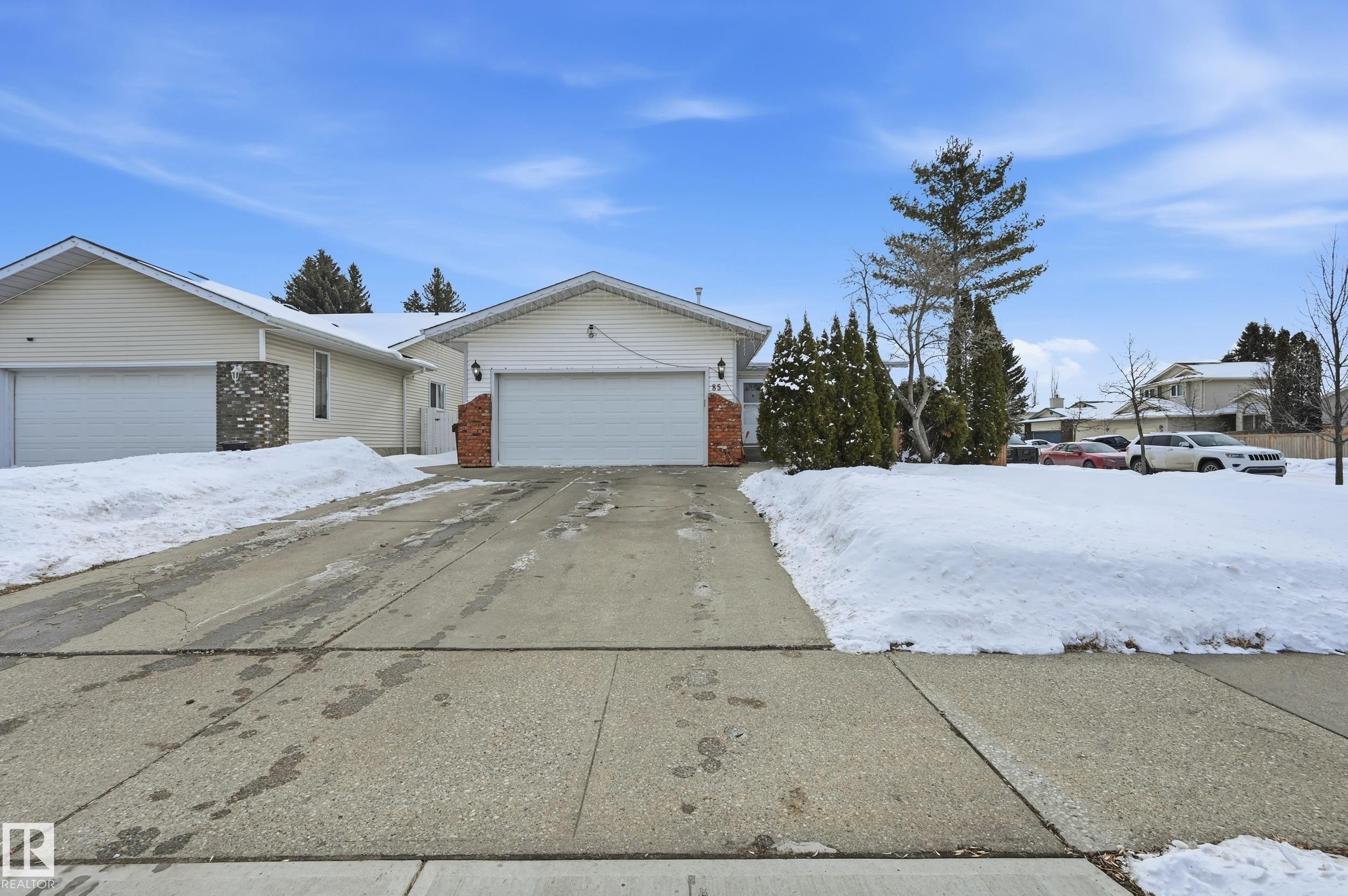 The property features a concrete driveway leading to an attached garage, with a partial brick facade accenting the front entrance - 85 Arlington Drive, St. Albert, AB - Outdoor