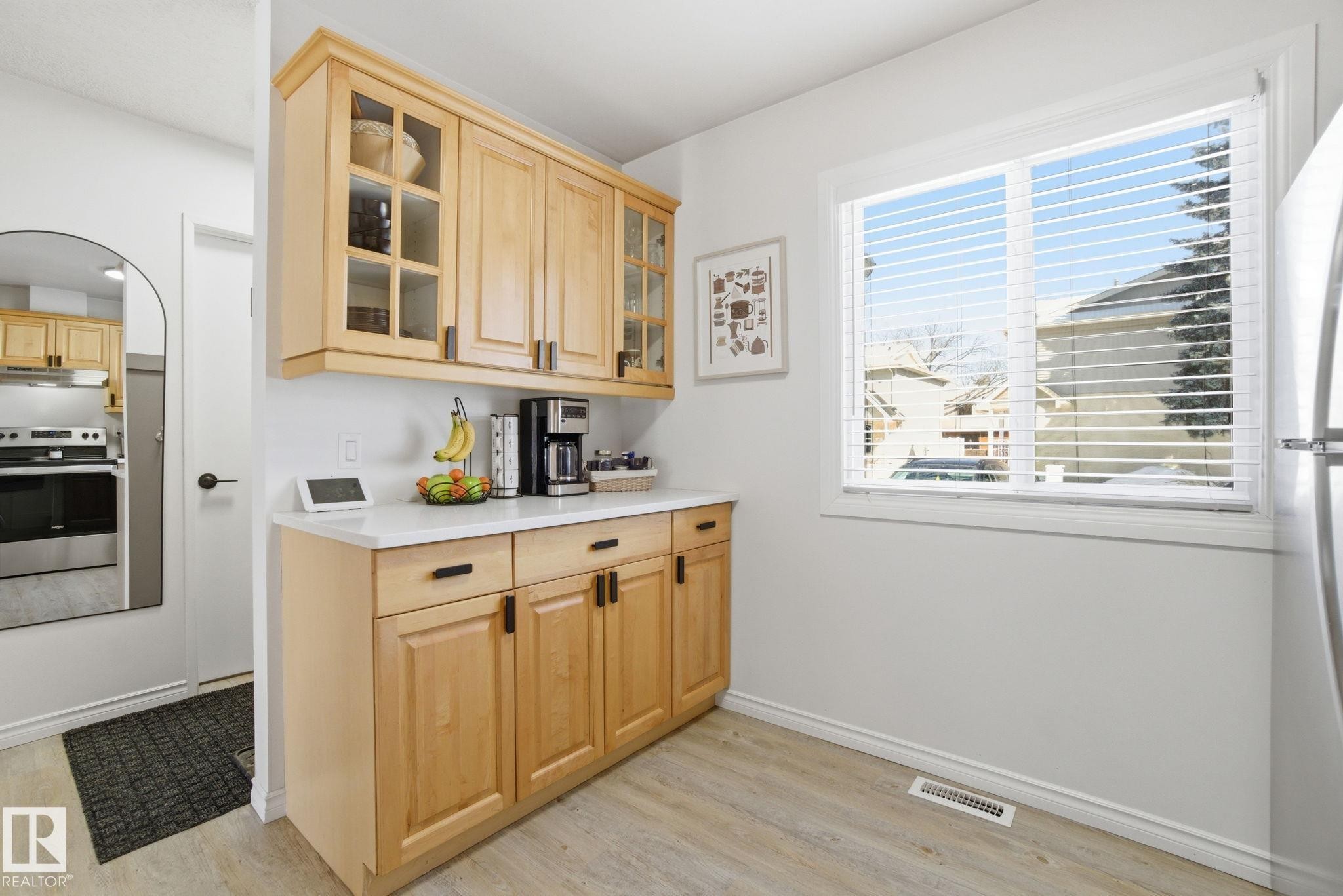 The kitchen features light wood cabinetry with dark hardware, a white countertop, and a window with horizontal blinds - 29 9619 180 Street, Edmonton, AB - Indoor Photo Showing Kitchen