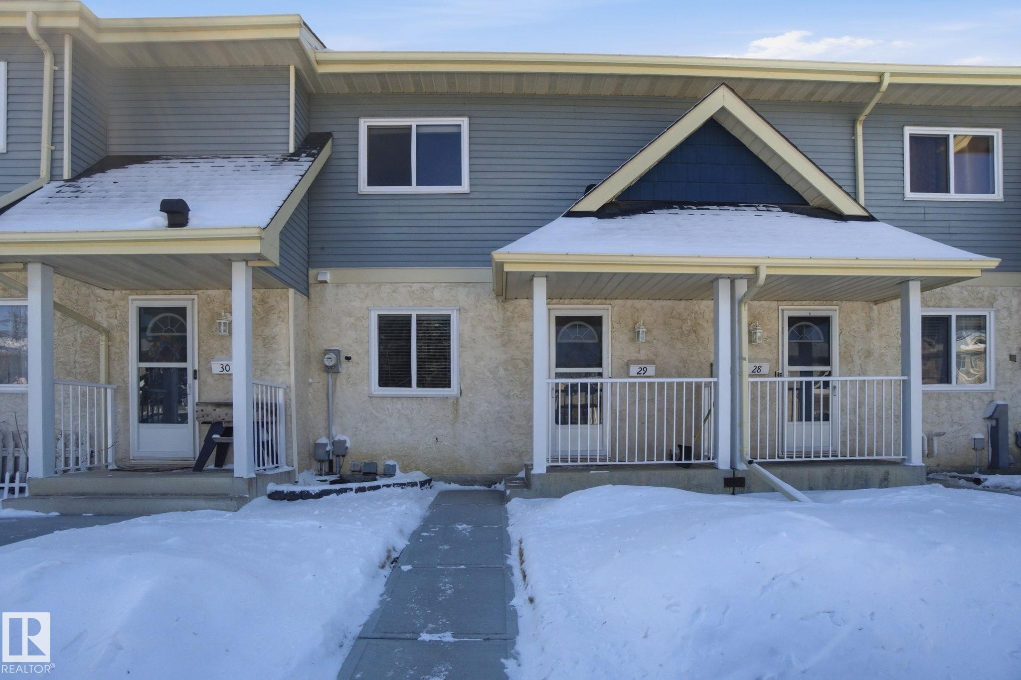 The property features a charming exterior with light blue siding and light stucco, complemented by white window frames and a covered front porch - 29 9619 180 Street, Edmonton, AB - Outdoor With Deck Patio Veranda With Facade