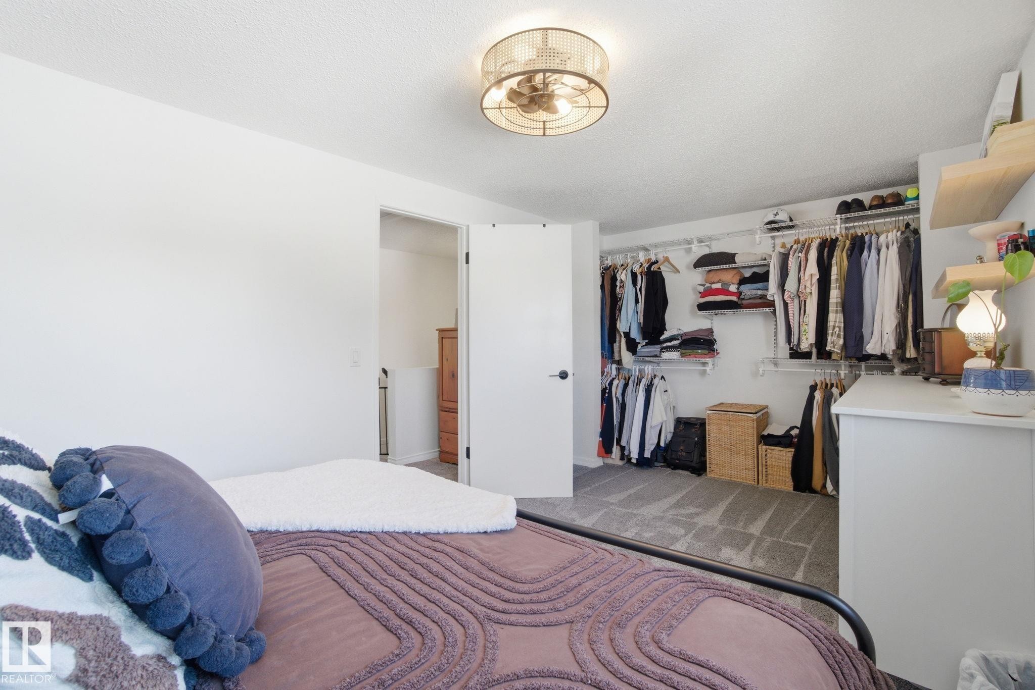 This bedroom features a ceiling light fixture with an integrated fan, a spacious closet with custom shelving, and light-colored carpeting - 29 9619 180 Street, Edmonton, AB - Indoor Photo Showing Bedroom