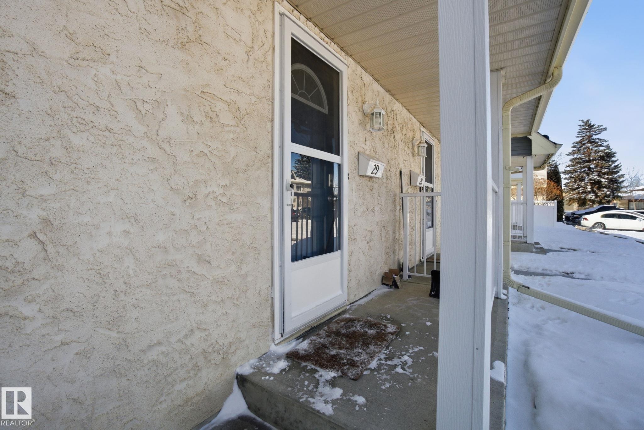 The property features a textured stucco exterior, a front door with an arched window insert, and a covered porch - 29 9619 180 Street, Edmonton, AB - Outdoor