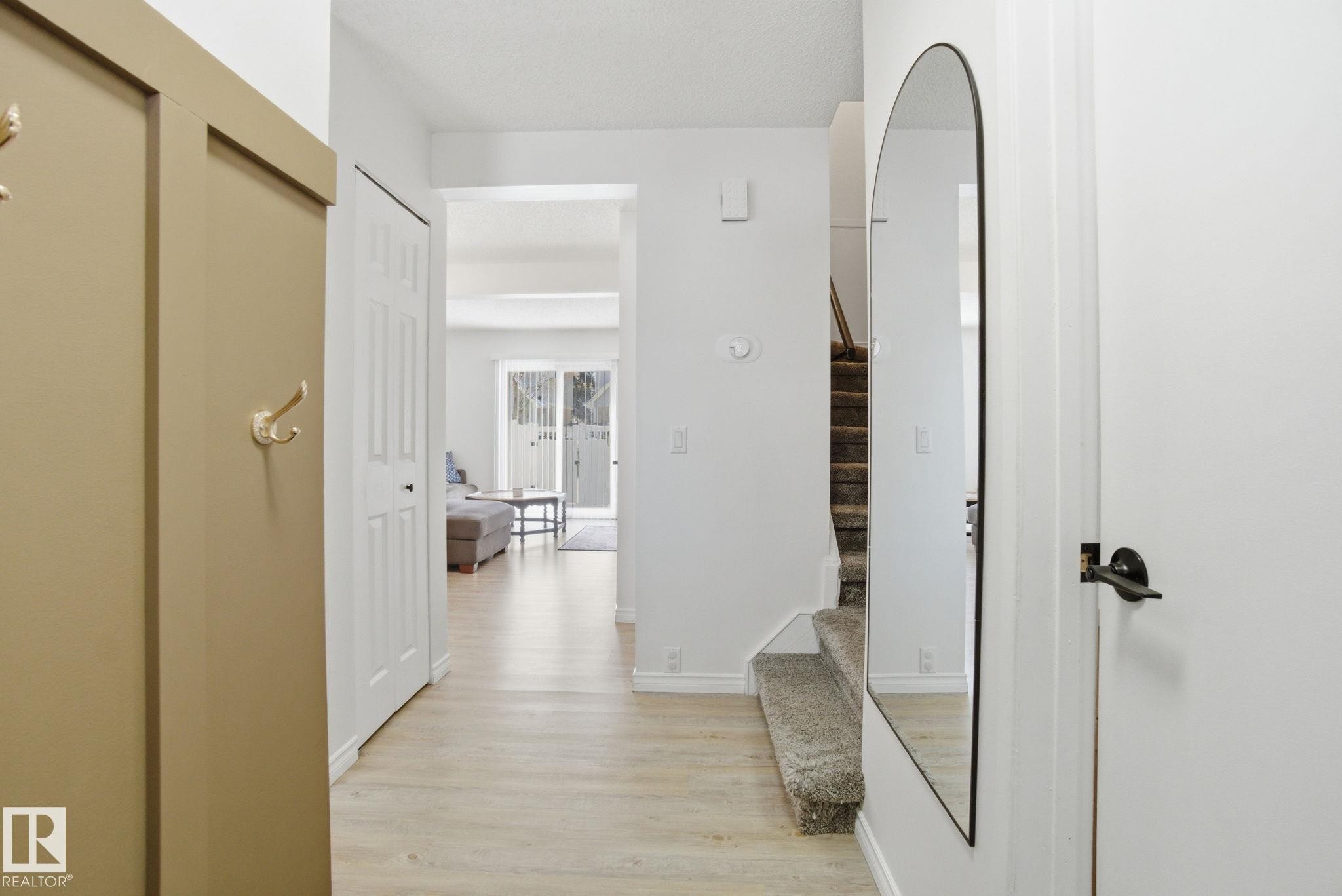 Entryway featuring light-toned flooring, a mirrored accent, and a view into an open living area with sliding glass doors - 29 9619 180 Street, Edmonton, AB - Indoor Photo Showing Other Room