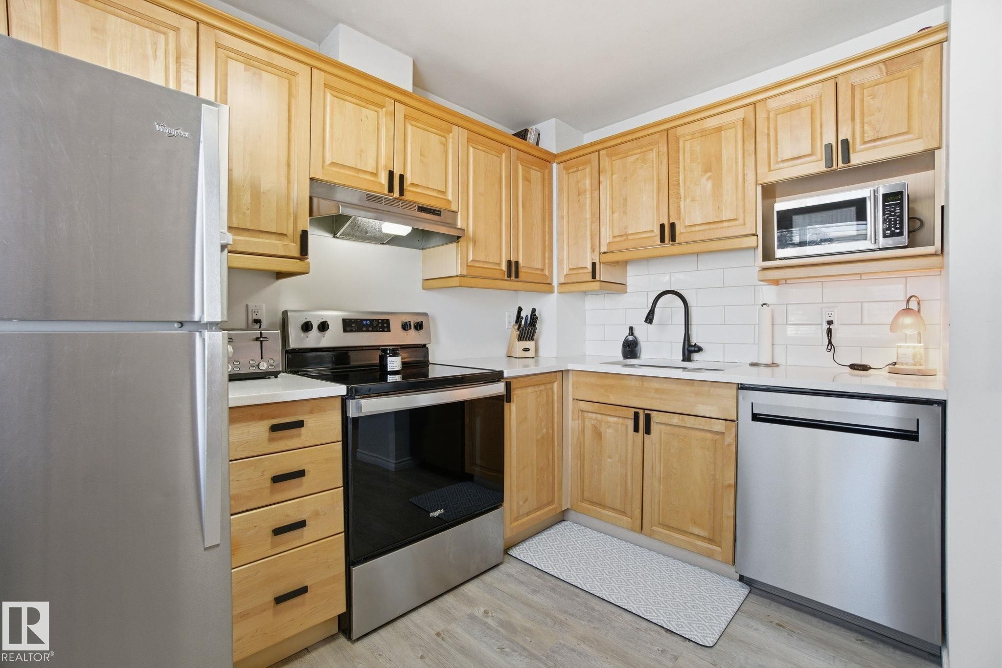 The kitchen features light wood cabinetry, stainless steel appliances, white countertops, and a white subway tile backsplash - 29 9619 180 Street, Edmonton, AB - Indoor Photo Showing Kitchen