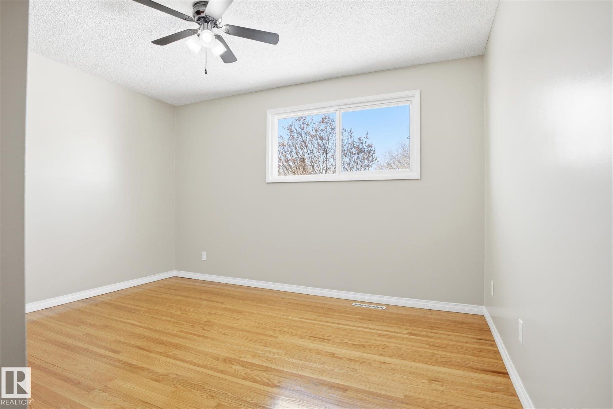 This room features hardwood floors, light-colored walls, a window with a view of trees and sky, and a ceiling fan with integrated lighting - 6 Garden Crescent, St. Albert, AB - Indoor Photo Showing Other Room