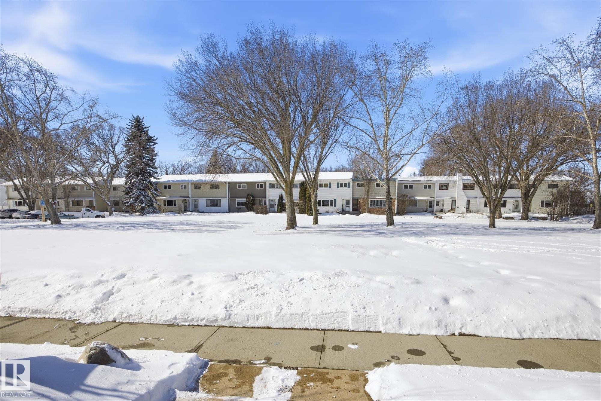 The property features a multi-unit residential building with light-colored siding and a contrasting roofline, set amidst mature trees - 6 Garden Crescent, St. Albert, AB - Outdoor