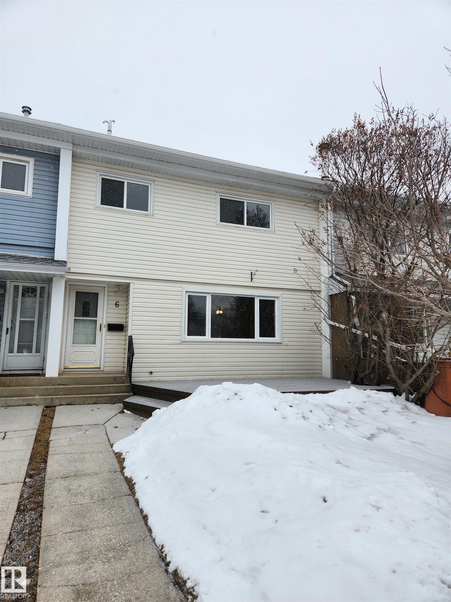 The property features light-colored horizontal siding, a front door with a window, and a concrete pathway leading to the entrance - 6 Garden Crescent, St. Albert, AB - Outdoor