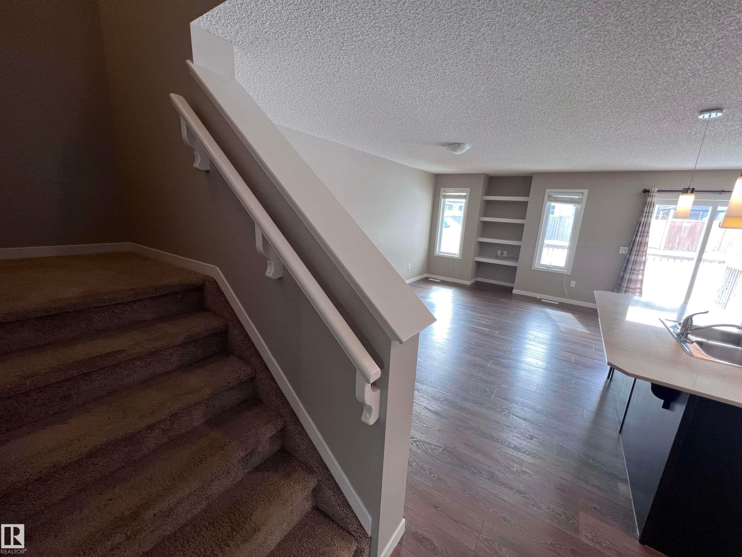 The property features a staircase with carpeted treads and a handrail, leading to a main living area with dark wood flooring - 1421 26 Avenue, Edmonton, AB - Indoor Photo Showing Other Room